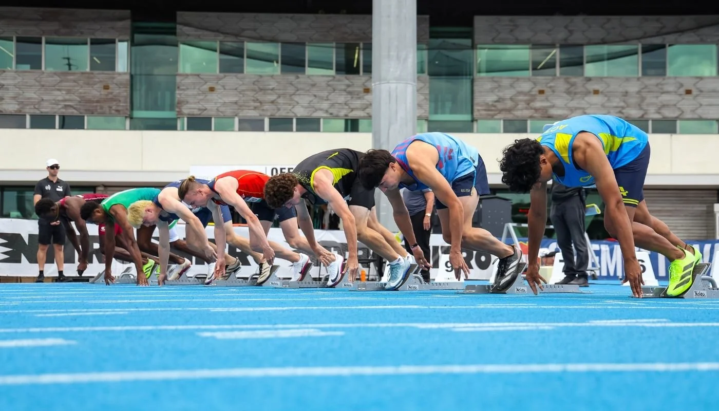 Sprinters in adjacent lanes beginning to push out of their starting blocks on a blue track.