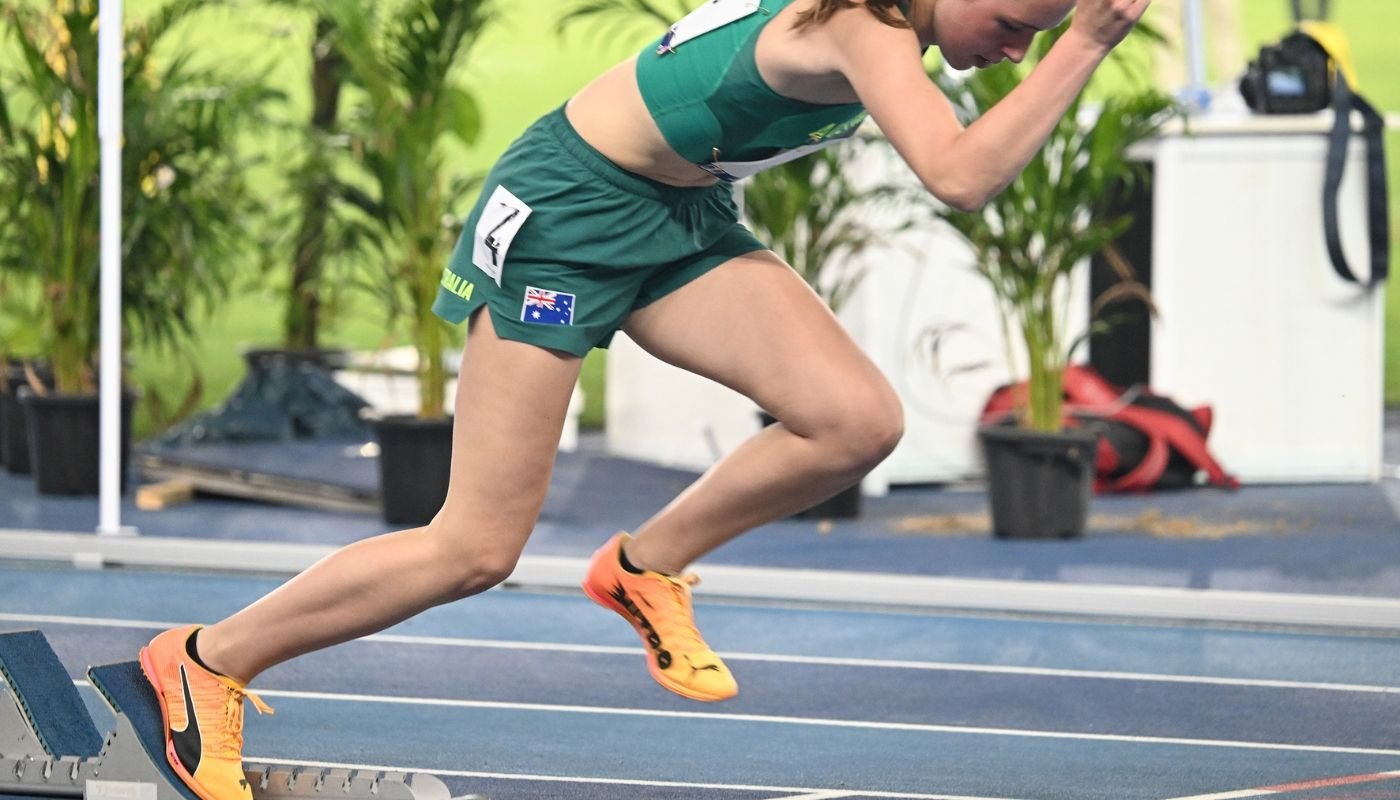 Australian sprinter driving out of the blocks, with the front leg extended against the footplate and the rear leg moving forwards into the first step.