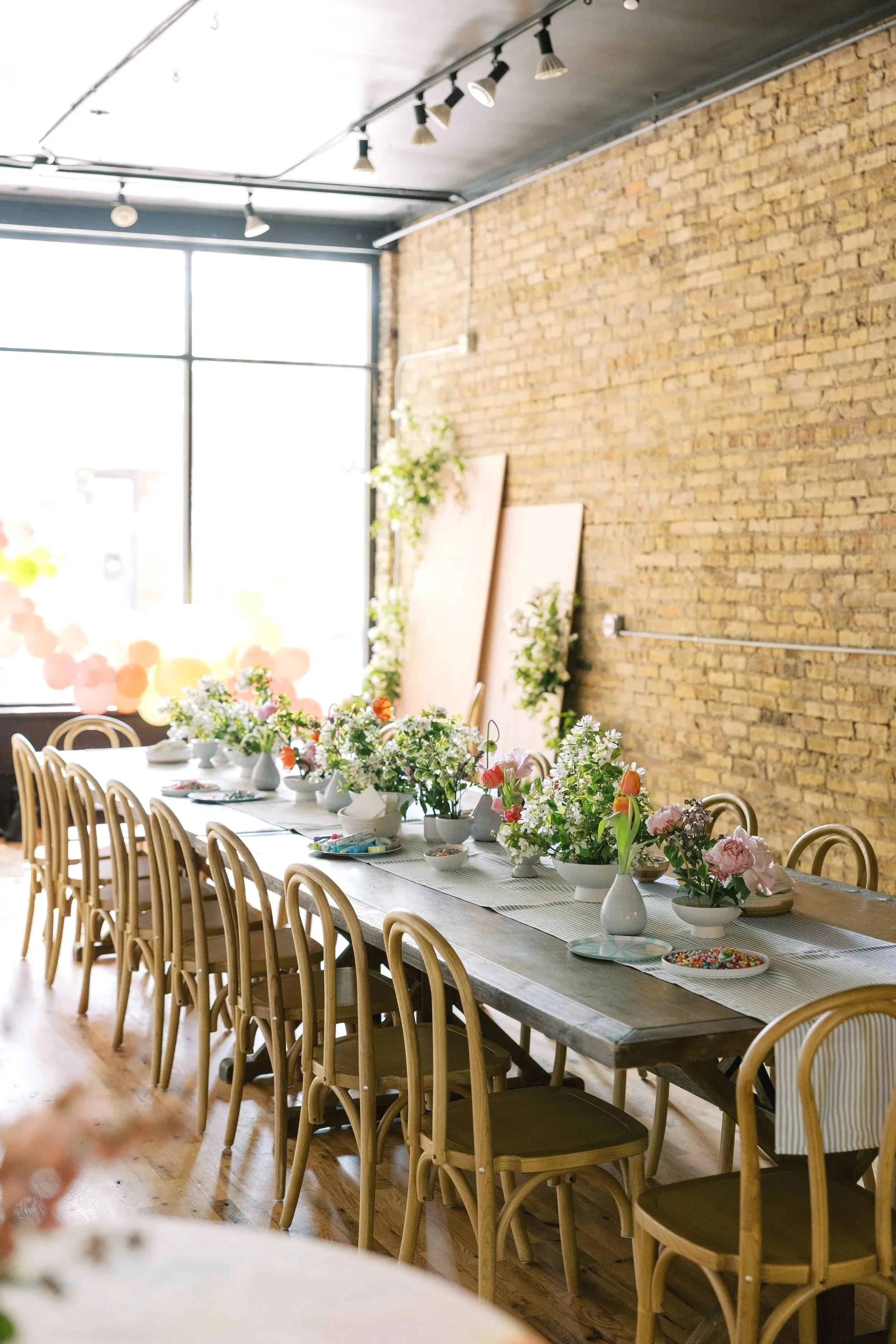 picture of event space with a long table with flowers, a backdrop, balloons, and wooden chairs