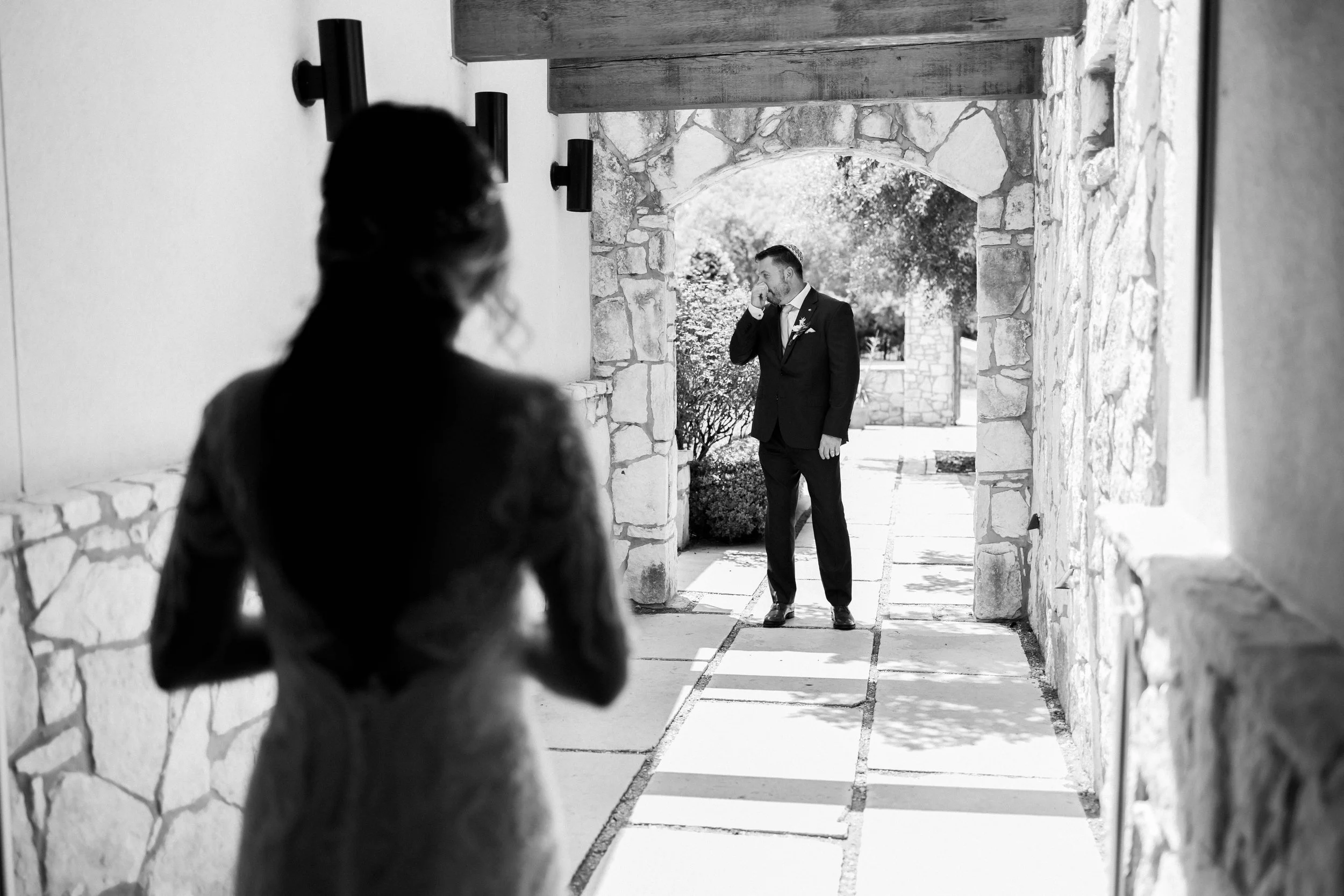 A woman in a wedding dress looking at a man in a tuxedo outside in a stone archway.