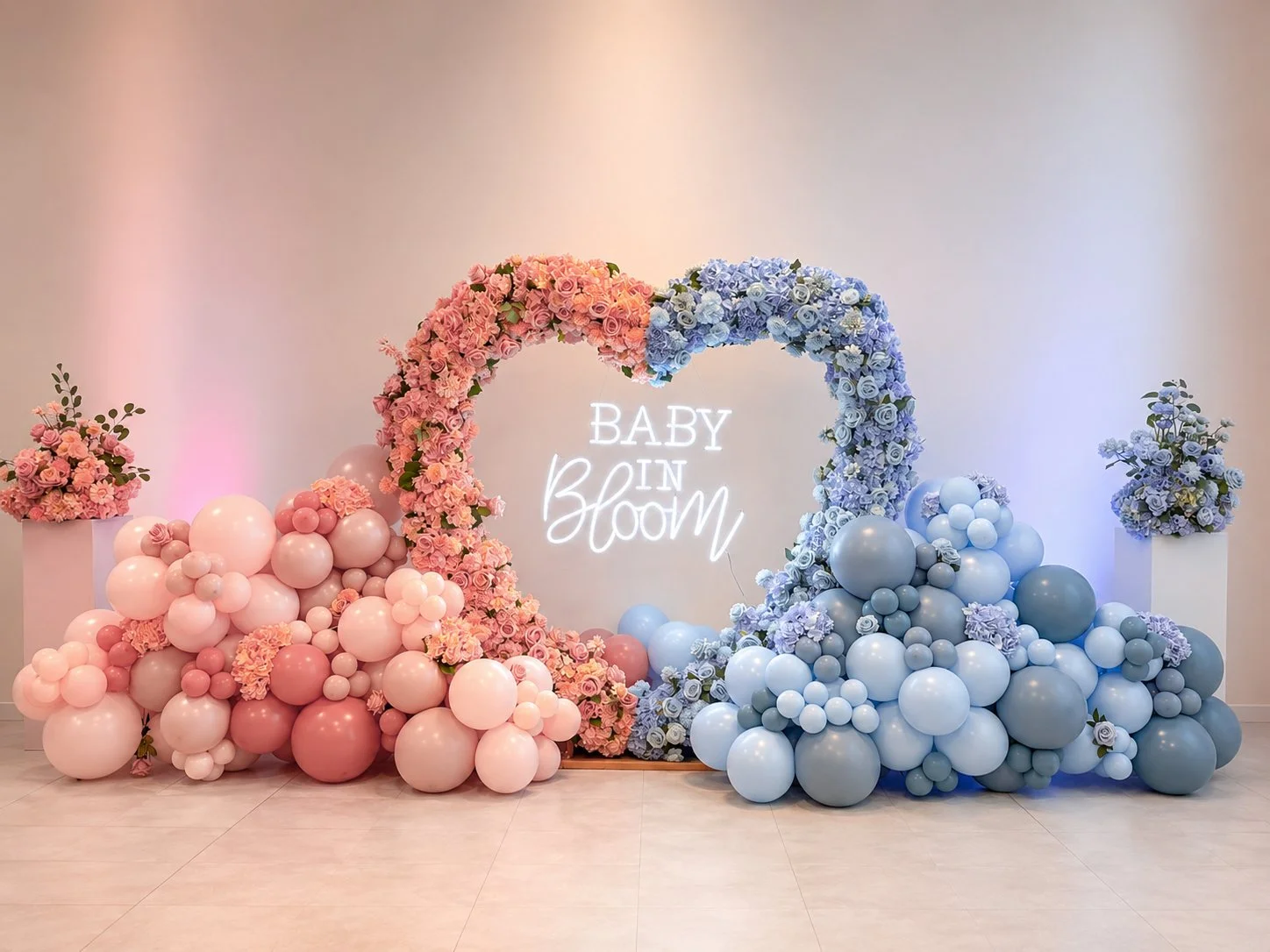 Balloon heart arch flower, half pink half blue, with balloons, half pink half blue and 'Baby in bloom' neon sign. 