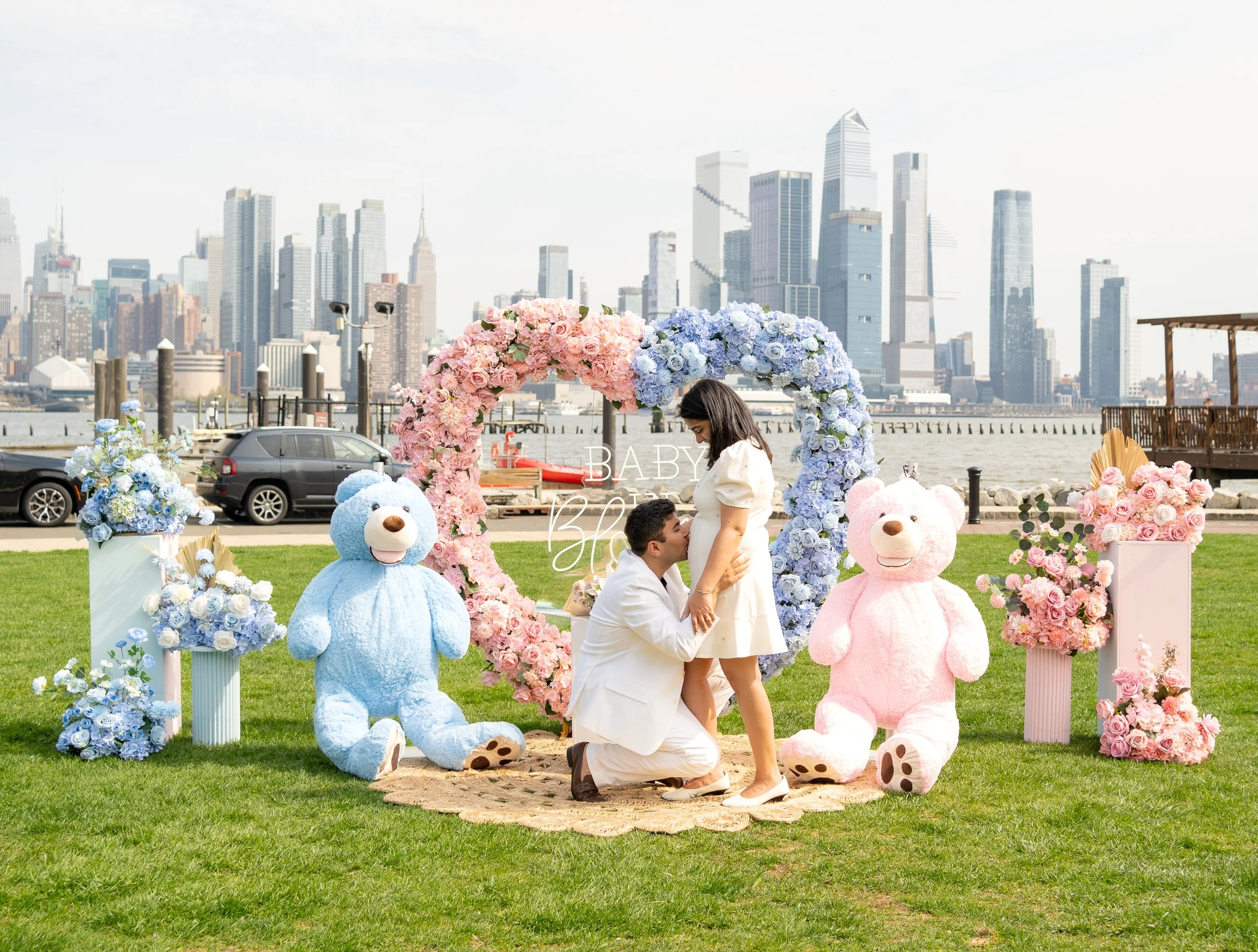 Heart arch, half pink half blue, with flower bouquets and teddy bears, with NY city sky line view 