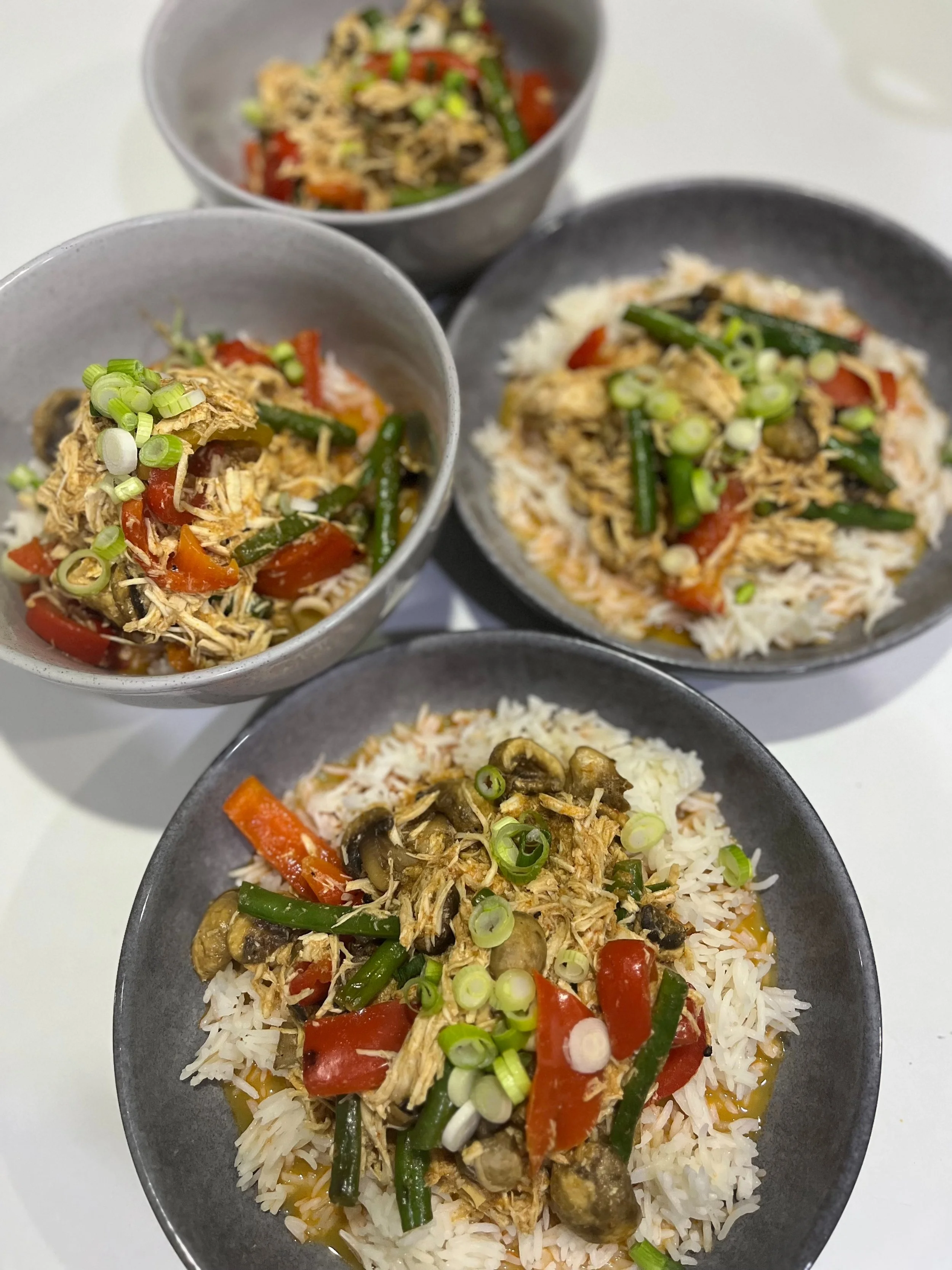 Bowls and plates of rice topped with shredded chicken, green beans, red bell peppers, mushrooms, and chopped green onions.
