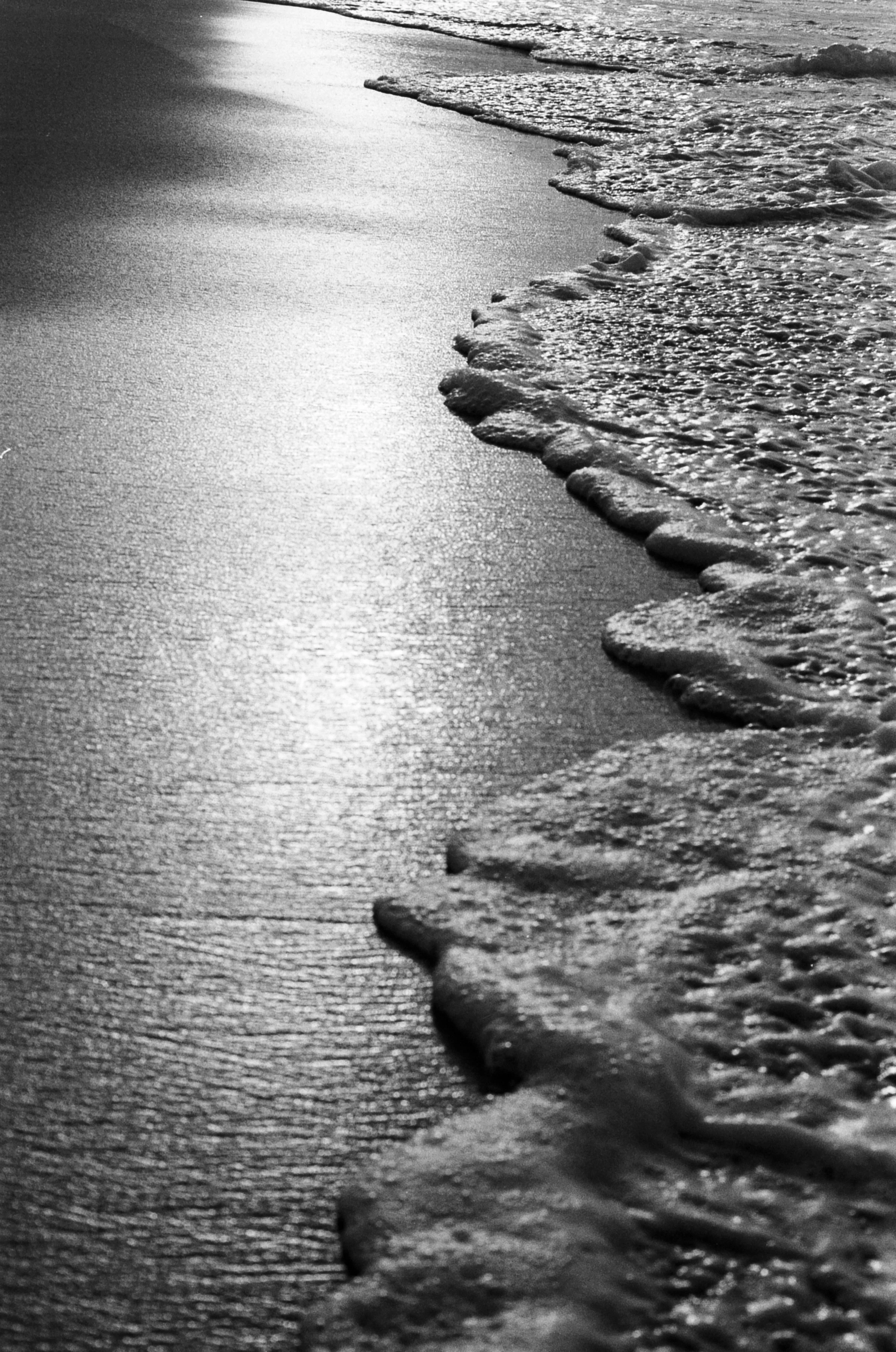 Black-and-white close-up of ocean waves washing onto a sandy beach