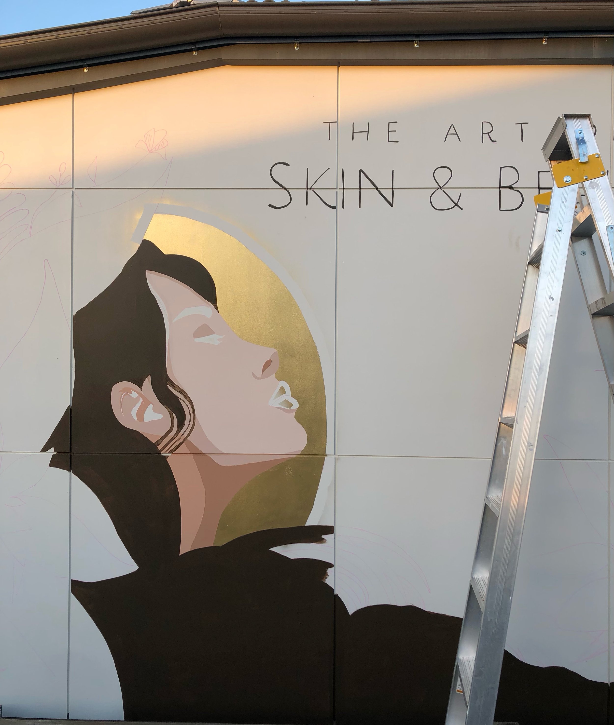 Mural artwork of a woman's face next to the text "The Art of Skin & Beauty" with a ladder on the right.
