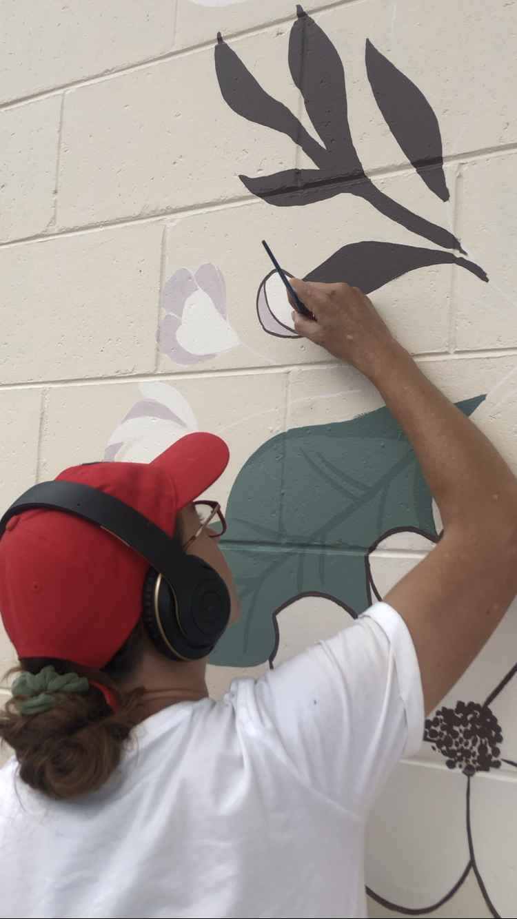 Person wearing a red cap and headphones painting a leaf mural on a brick wall.