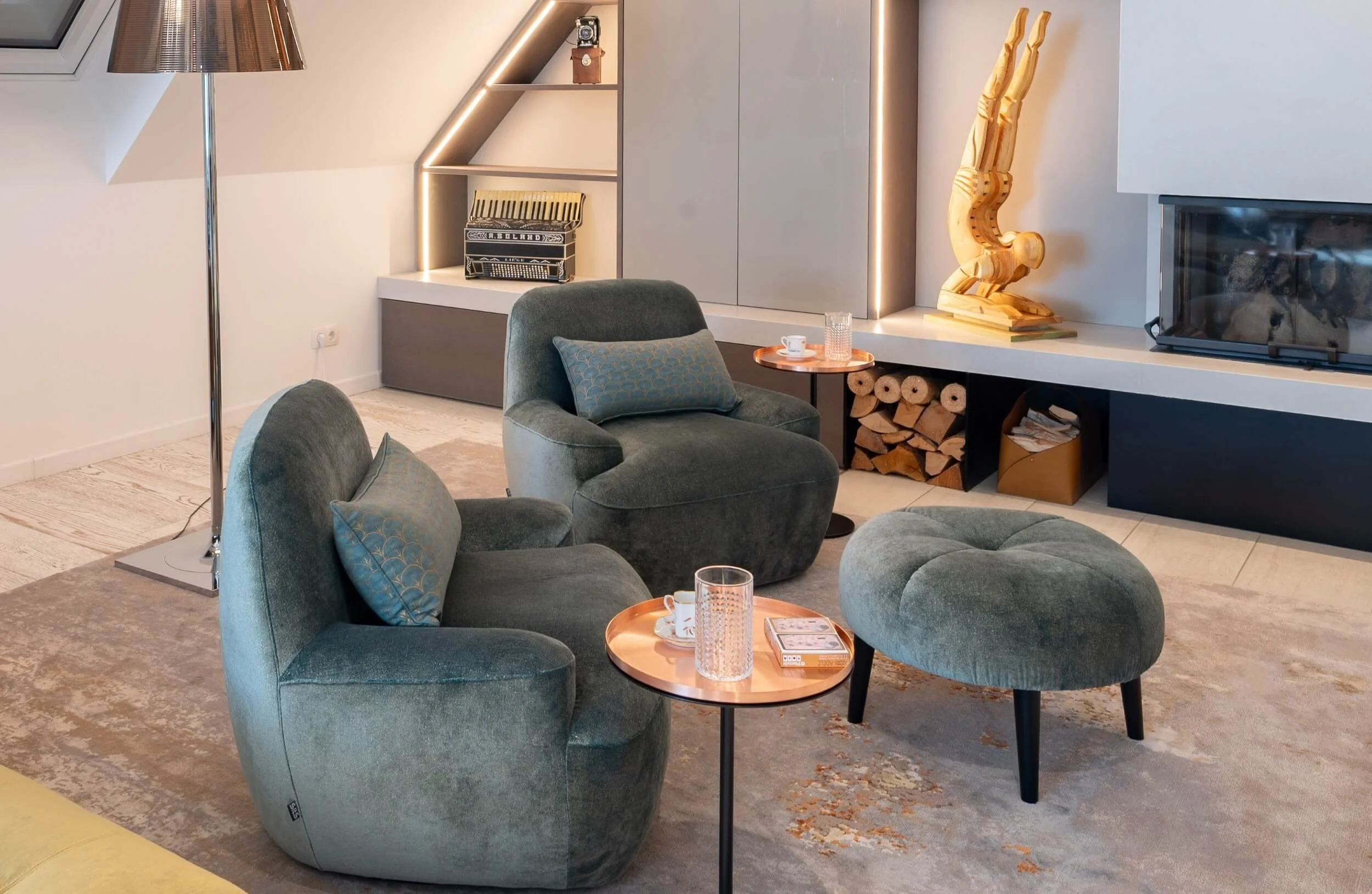 Gemütlicher Lesebereich mit zwei petrolfarbenen Fauteuils, Hocker, Beistelltischen und maßgefertigtem Einbau rund um den Kamin.