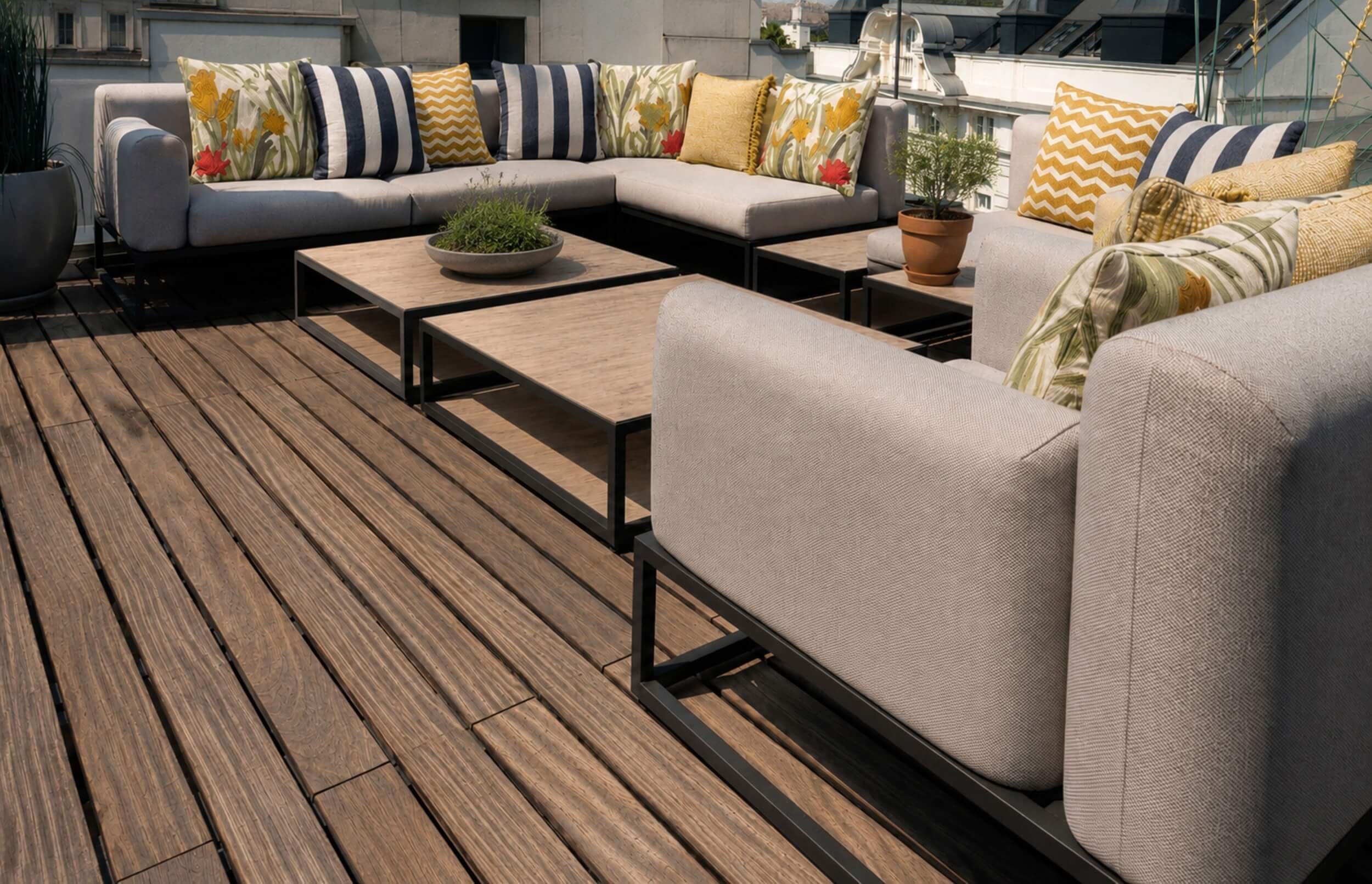 Großzügige Outdoor-Lounge auf der Wiener Dachterrasse mit modularer Sitzgruppe, gemusterten Kissen, niedrigen Couchtischen und urbanem Ausblick.