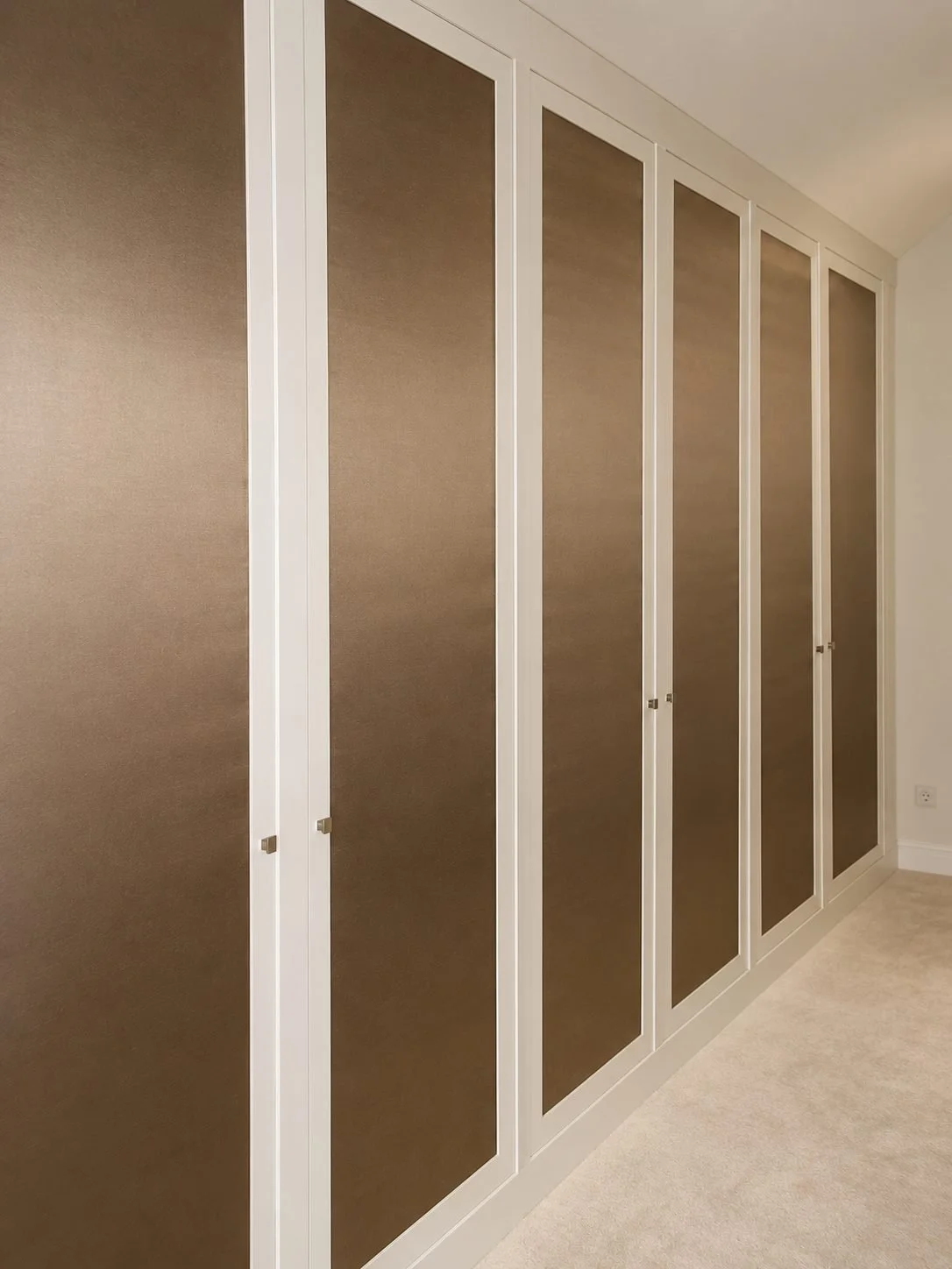 Maßgefertigte weiße Schrankfront mit hohen, braun bespannten Türfüllungen in Kunstleder und dezenten Metallgriffen in einem eleganten Schlafzimmer.