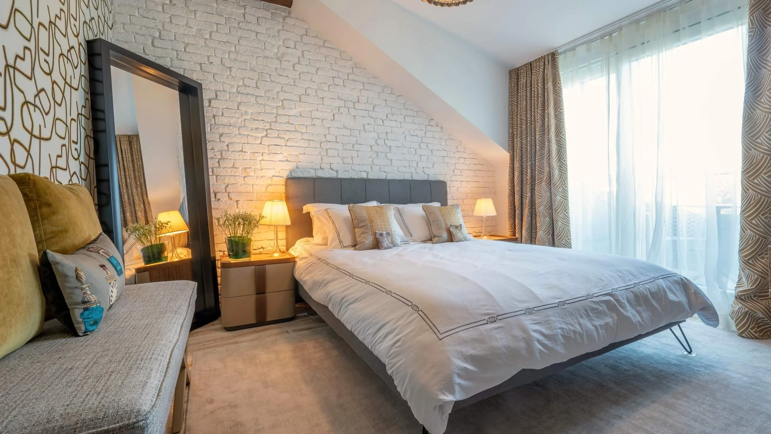 Individuell gestaltetes Schlafzimmer im Rooftop Apartment in 1060 Wien mit weißer Ziegelwand, grafischer Tapete, gepolstertem Bett und Zugang zur Terrasse.