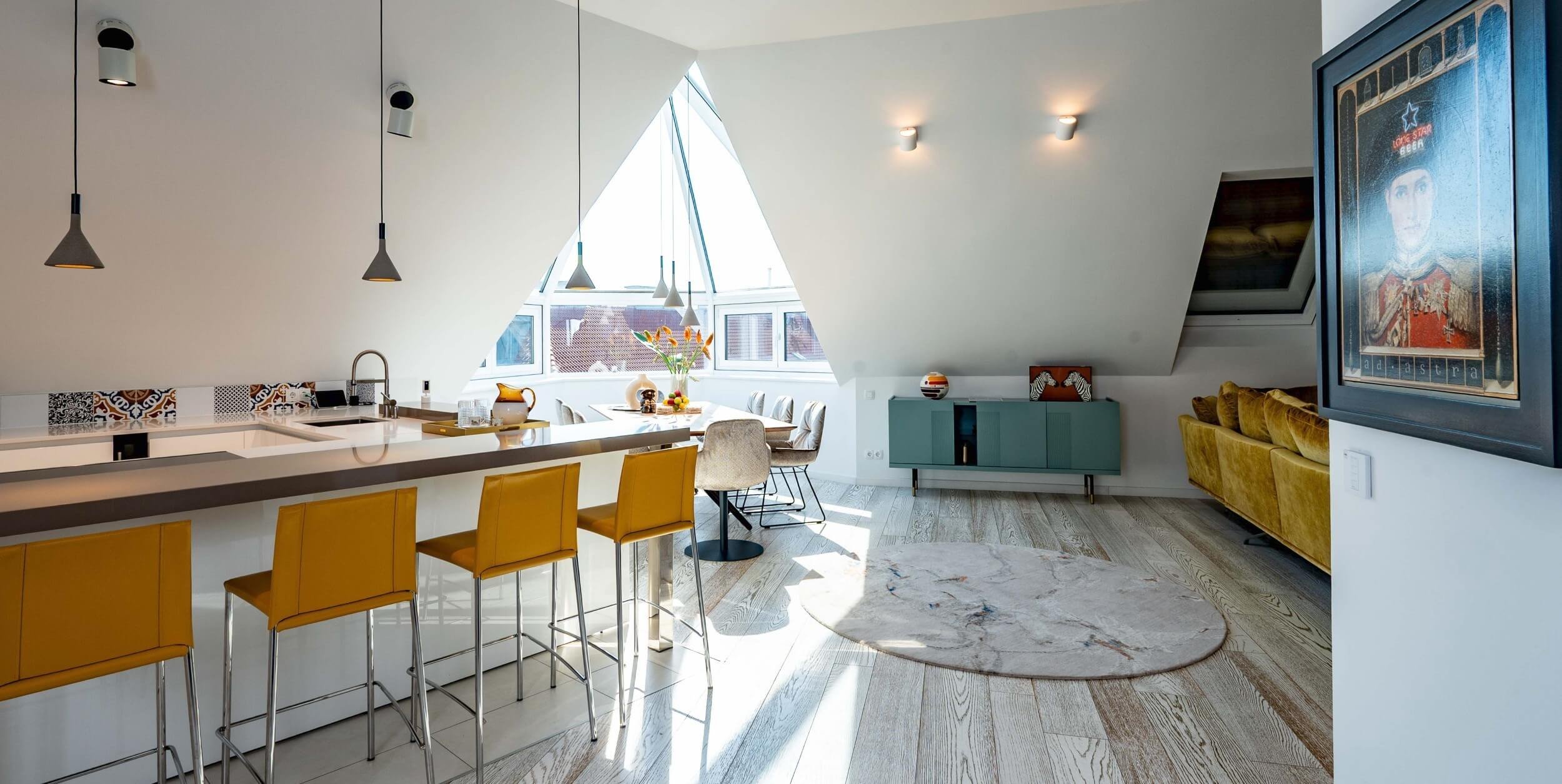 Offene weiße Küche im Rooftop Apartment in 1060 Wien mit großzügiger Kochinsel, senfgelben Barhockern und grafisch gestaltetem Fliesenspiegel.