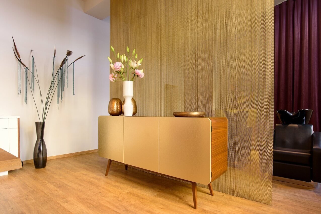 Sideboard with walnut and metal surface in front of metal chain veil - interior design with material contrast.