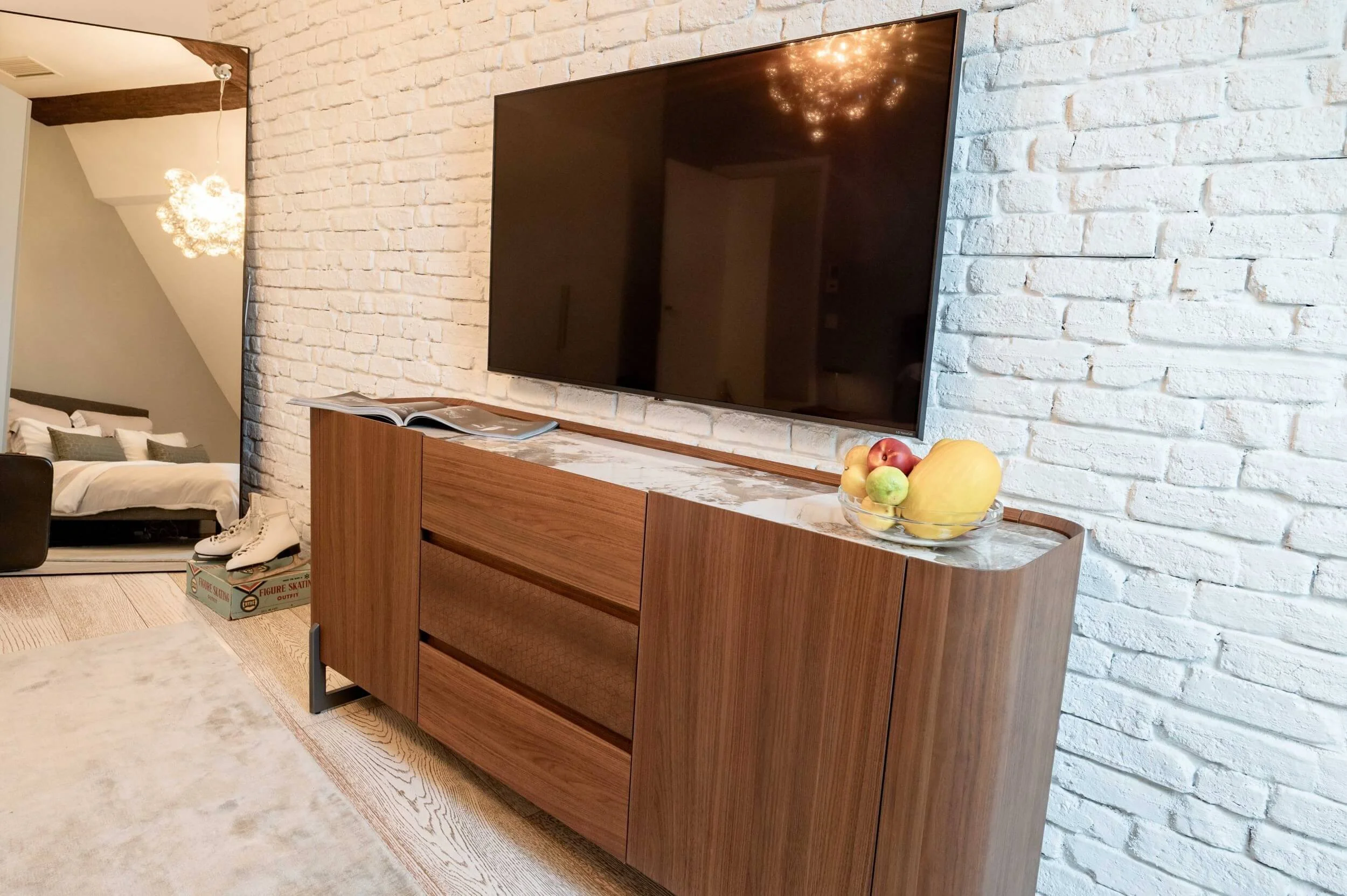TV-Kommode aus Holz mit heller Steinplatte vor einer weiß gestrichenen Ziegelwand im individuell eingerichteten Gästezimmer.