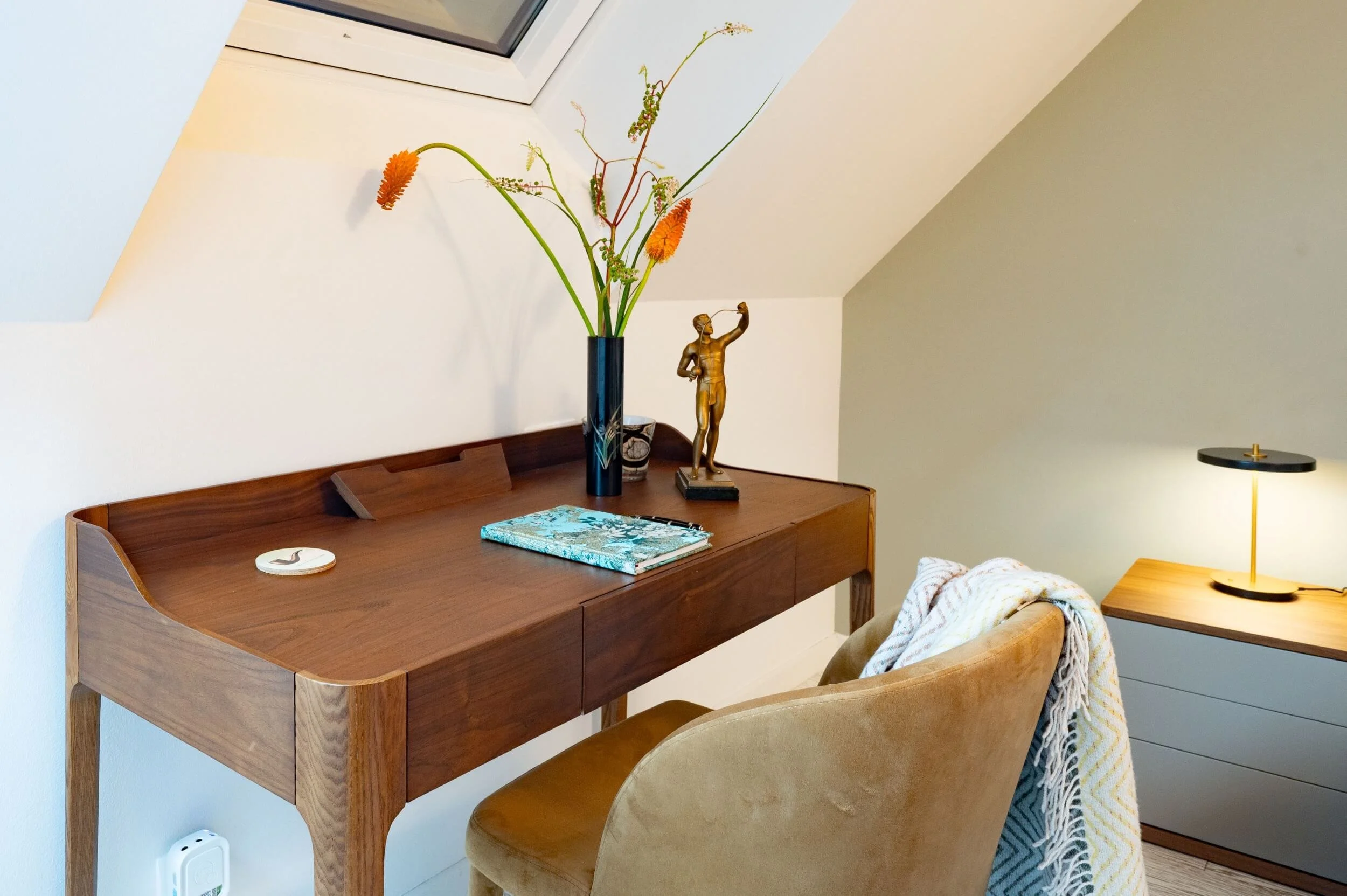 Arbeitsplatz im Gästezimmer mit elegantem Holzsekretär, gepolstertem Stuhl, Dachflächenfenster und ausgewählten Designobjekten.