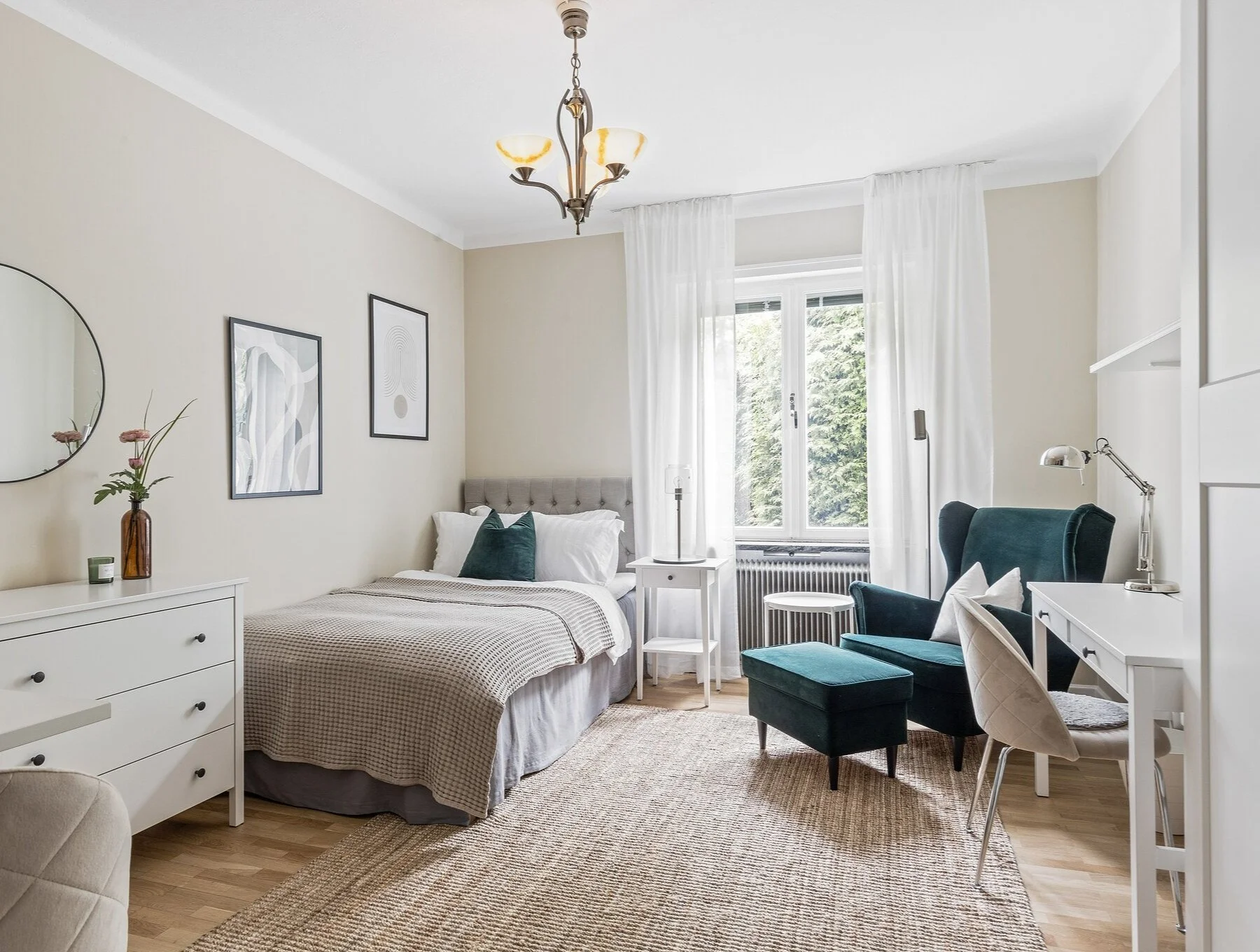 Cosy and light interior of bedroom with armchair, bed, desk and dresser