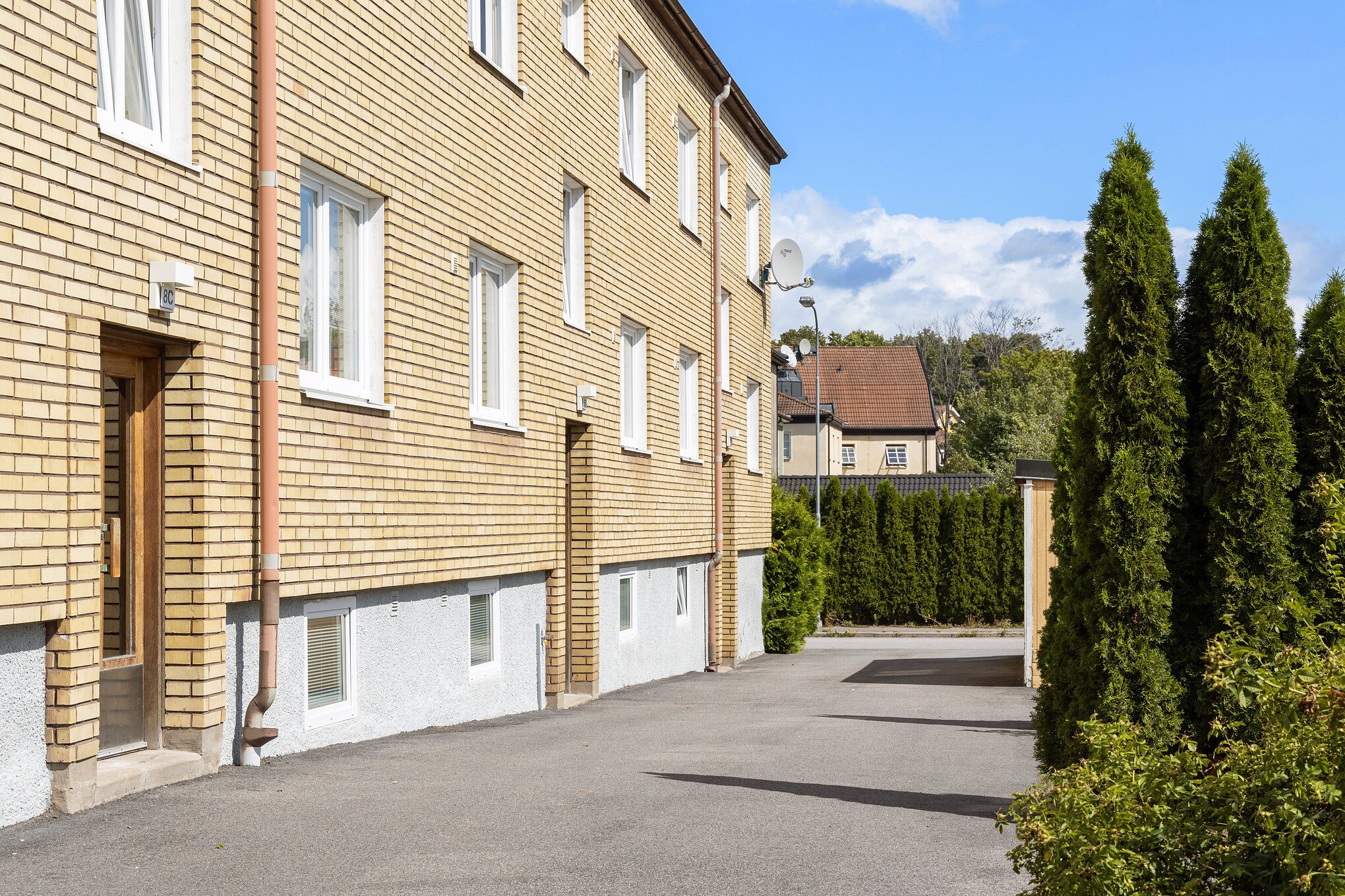 Image of apartment house exterior. Sandy coloured brick building in very sunny, lush green area in summer time.