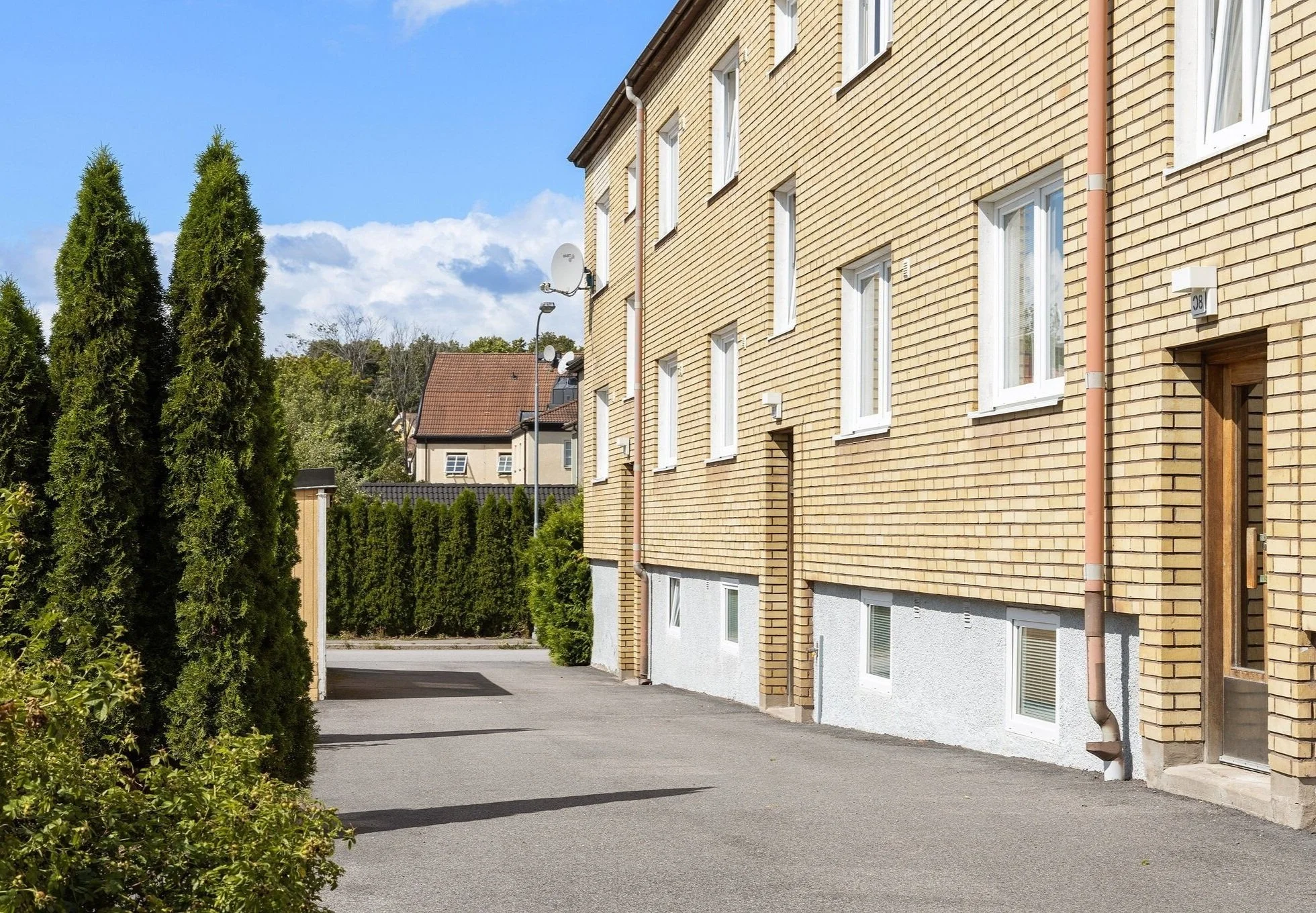 Image of apartment house exterior. Sandy coloured brick building in very sunny, lush green area in summer time.