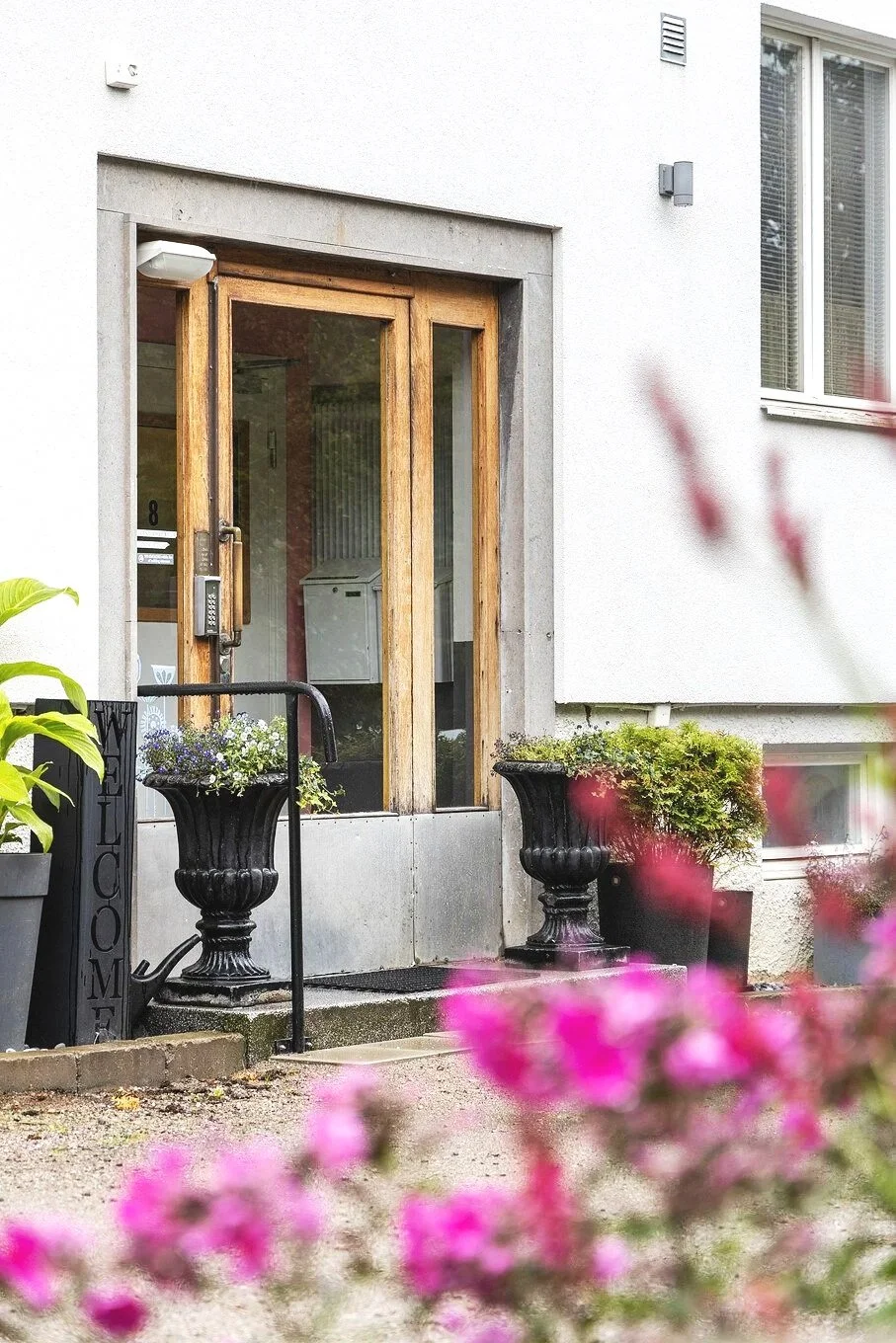 Nice view of door entrance to apartment building in summertime with green potted plants