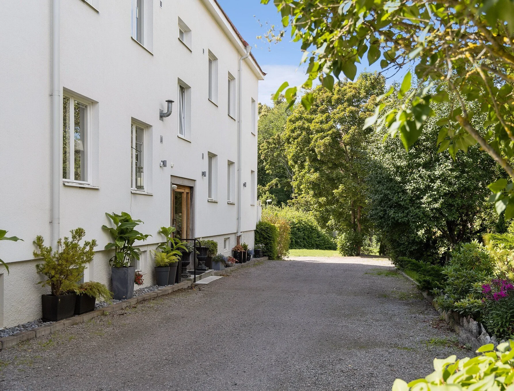 Image of apartment house exterior. White stone building in very sunny, lush green area in summer time.