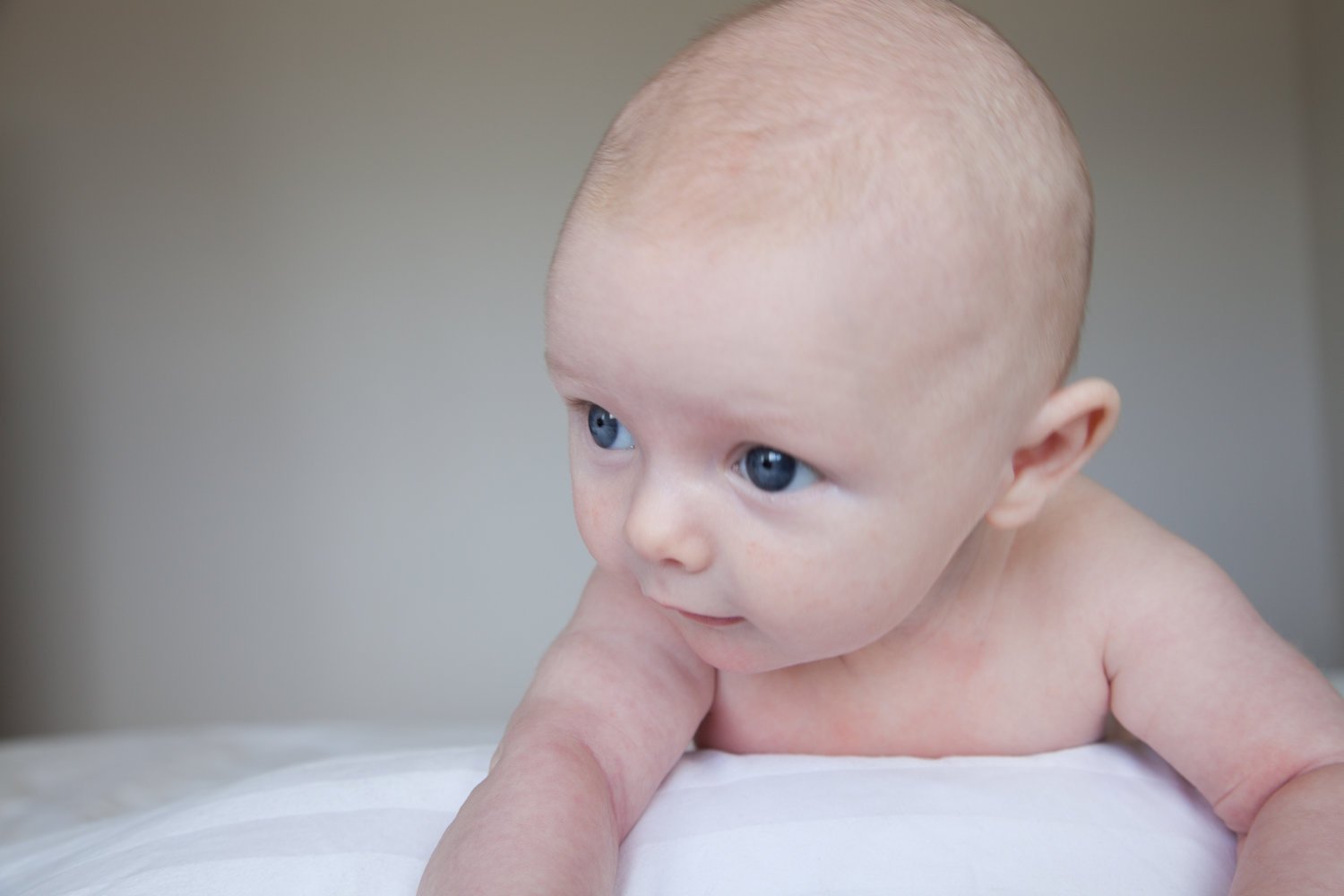 Close-up of a baby with blue eyes, lying on a white surface, looking to the side.
