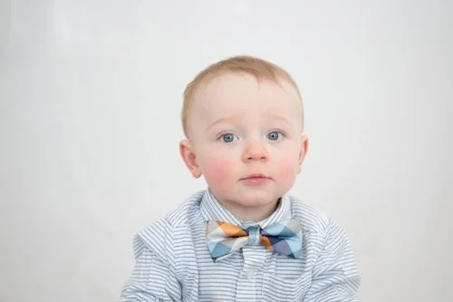 A young boy with light hair and blue eyes wearing a striped shirt and a bow tie.