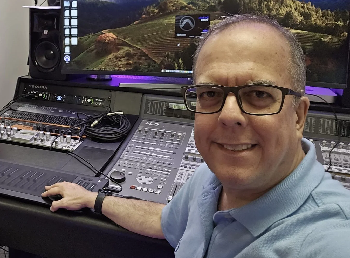 A man wearing glasses and a light blue polo shirt smiling at the camera against a white background.