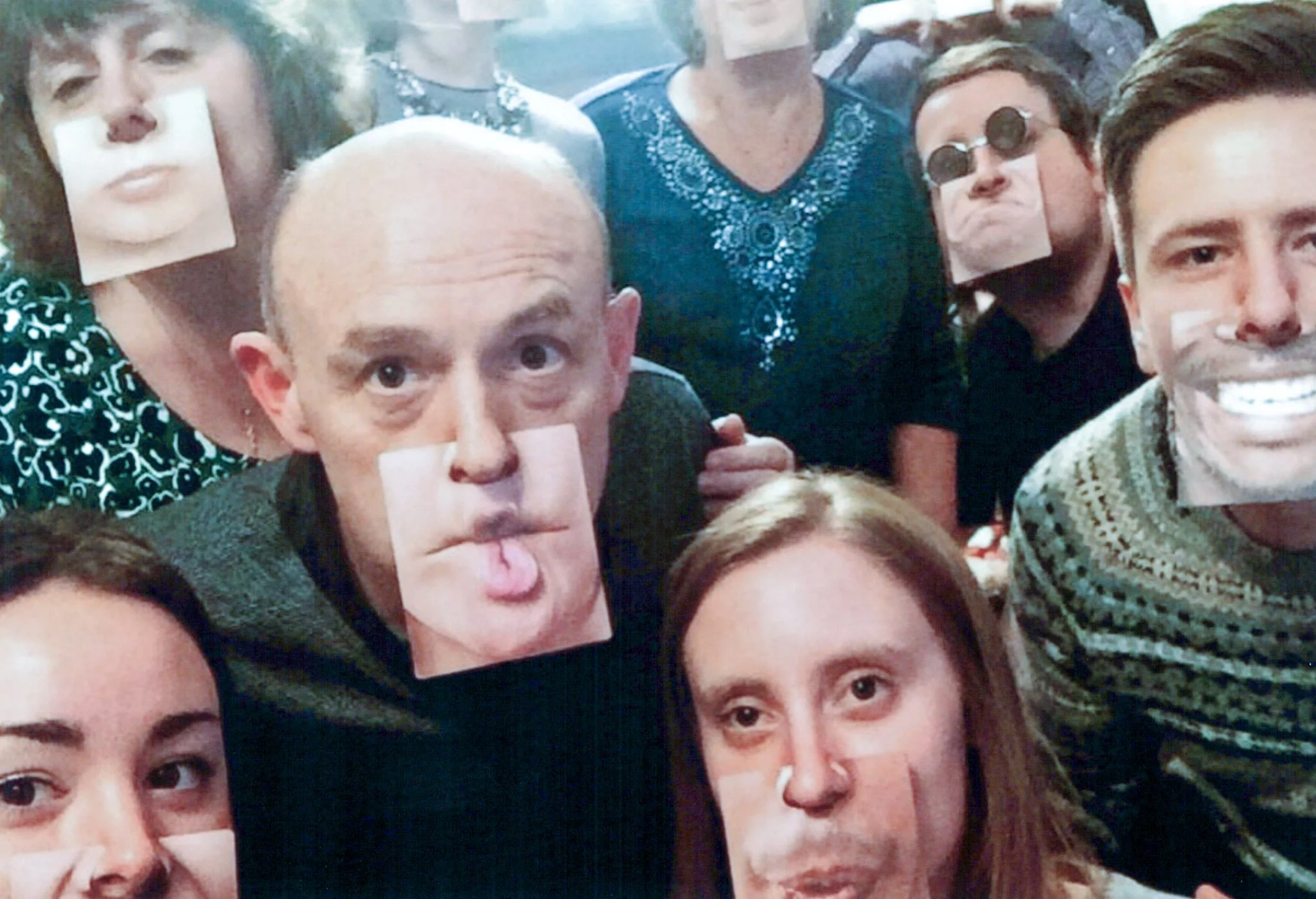 Group of people wearing face masks with cutouts of facial features, taking a selfie together.