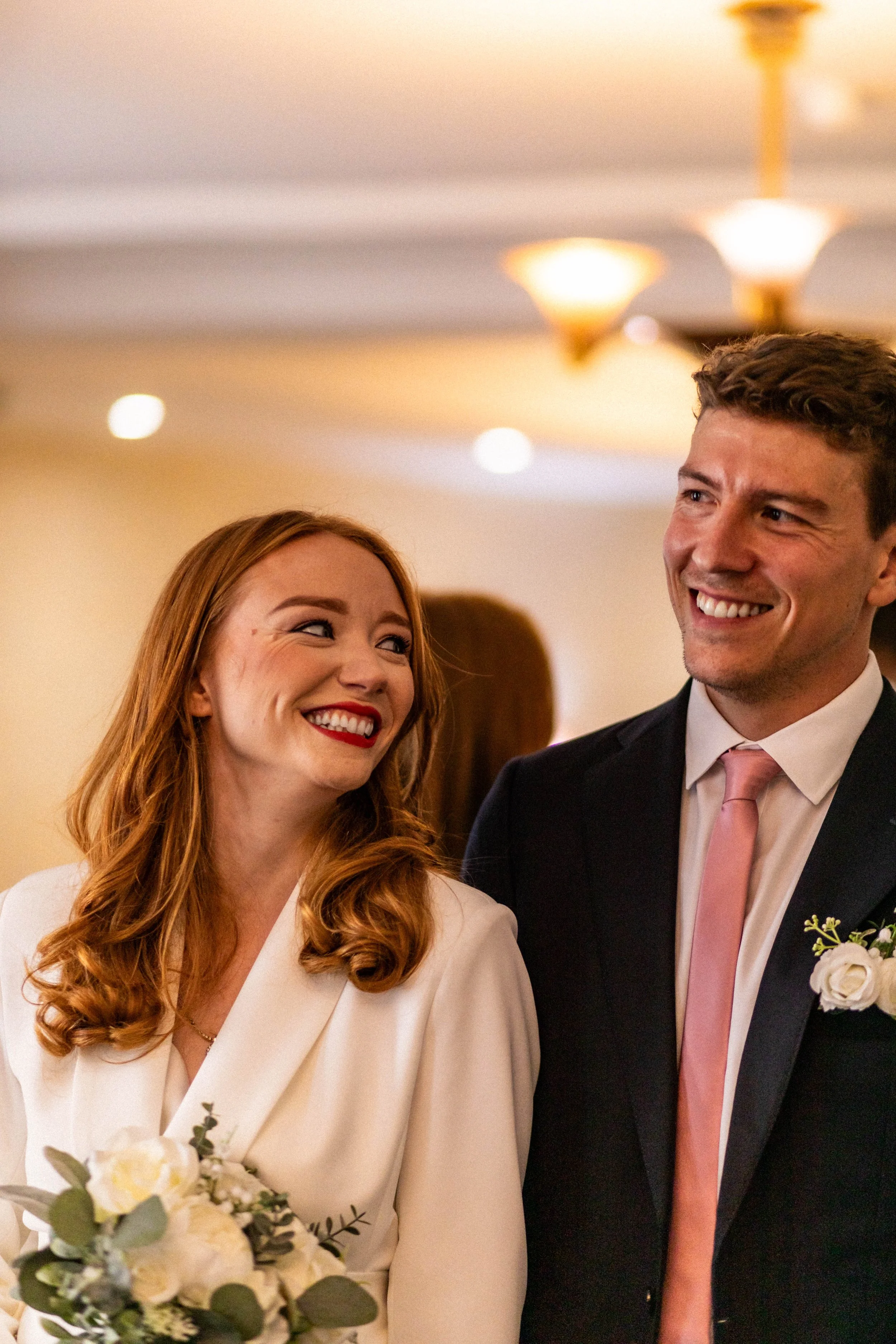 A bride and groom smiling at each other during their wedding celebration in an indoor venue.