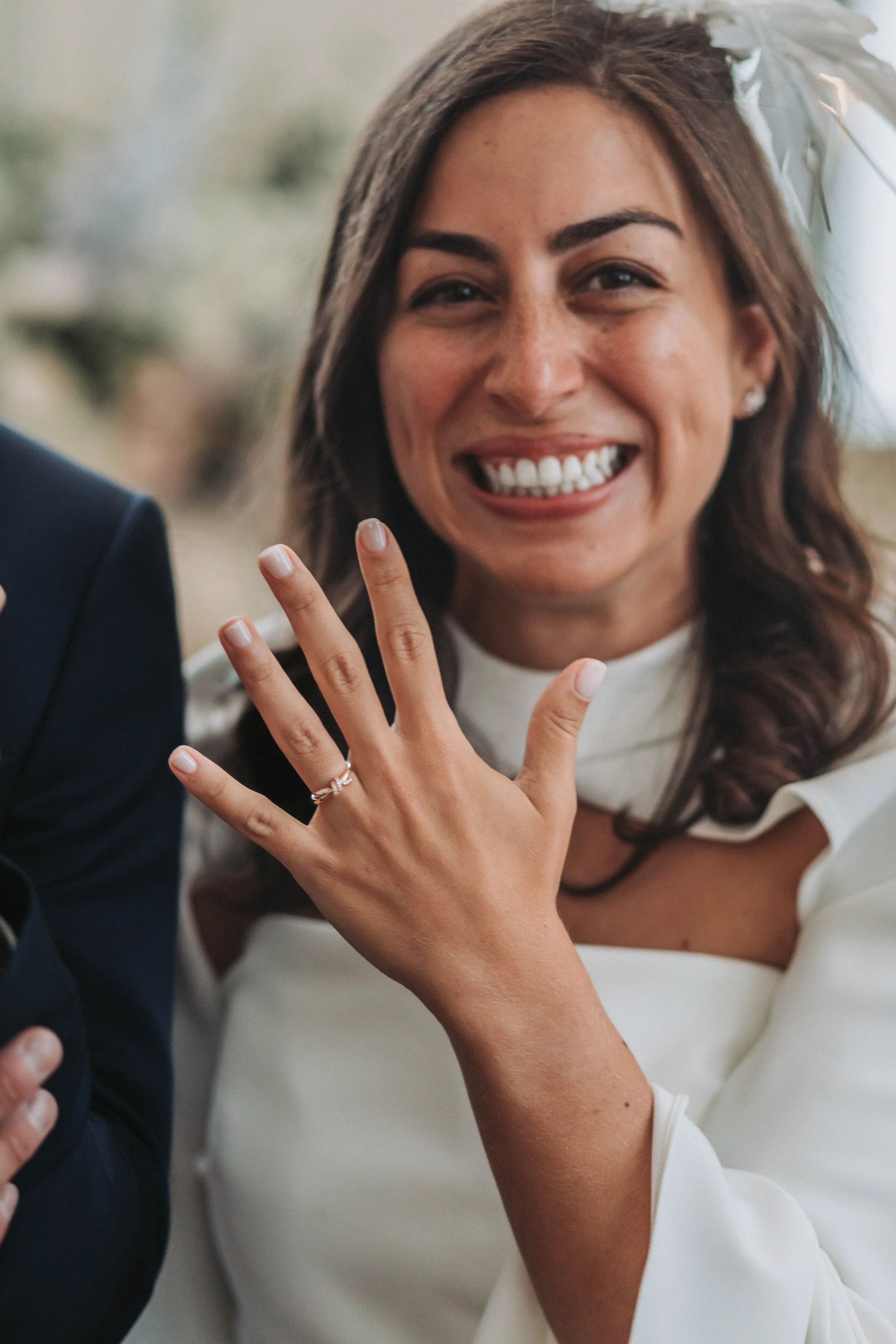 A woman is smiling and showing off her wedding ring on her left hand, during her wedding celebration.
