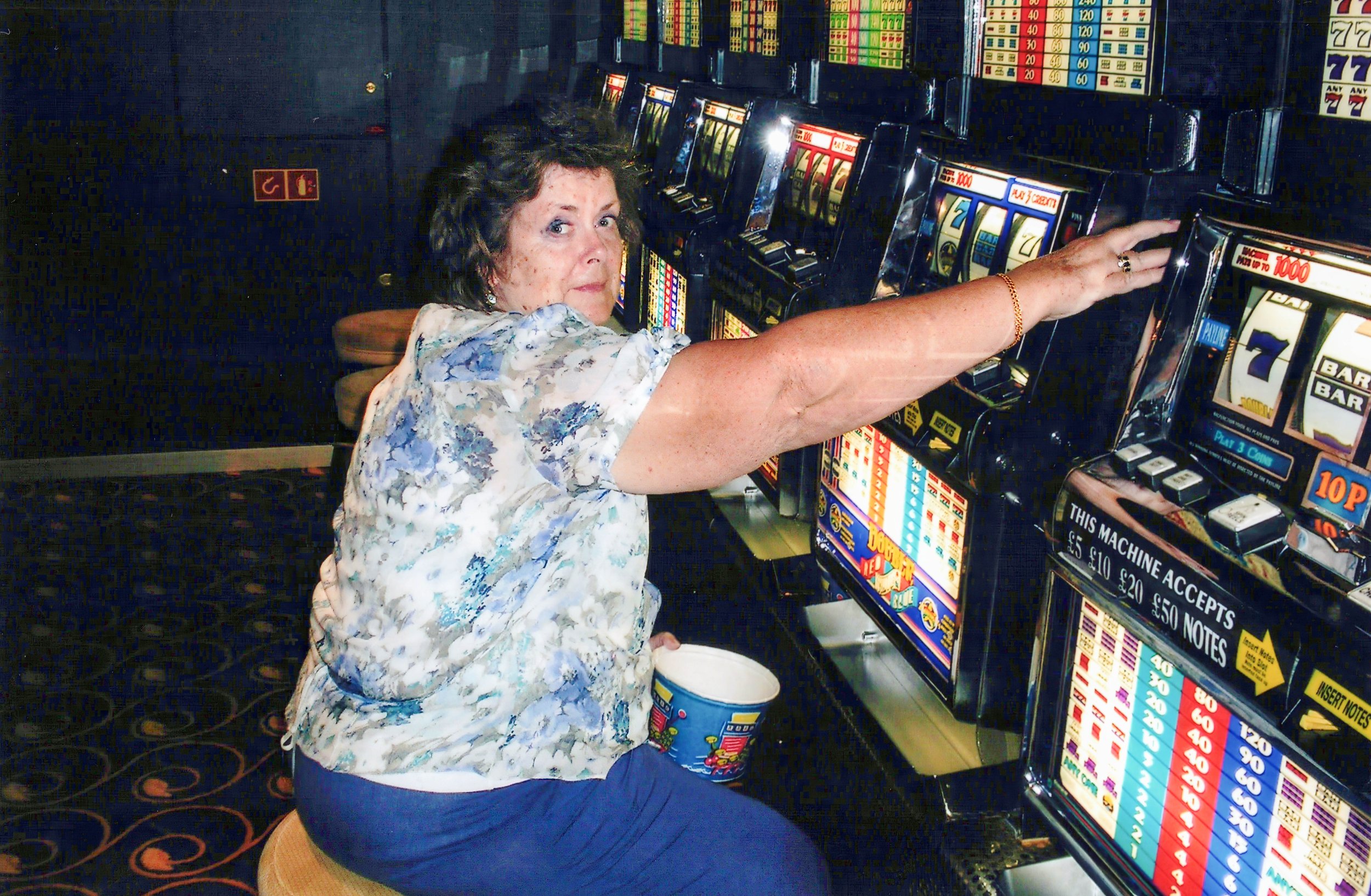 Person playing a slot machine in a casino, holding a cup.