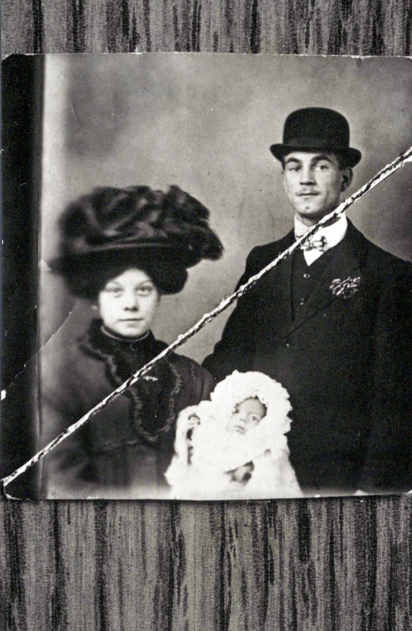 Black and white family portrait of a woman, a man, and a baby, with the woman wearing a large hat and the man in a suit and bow tie.