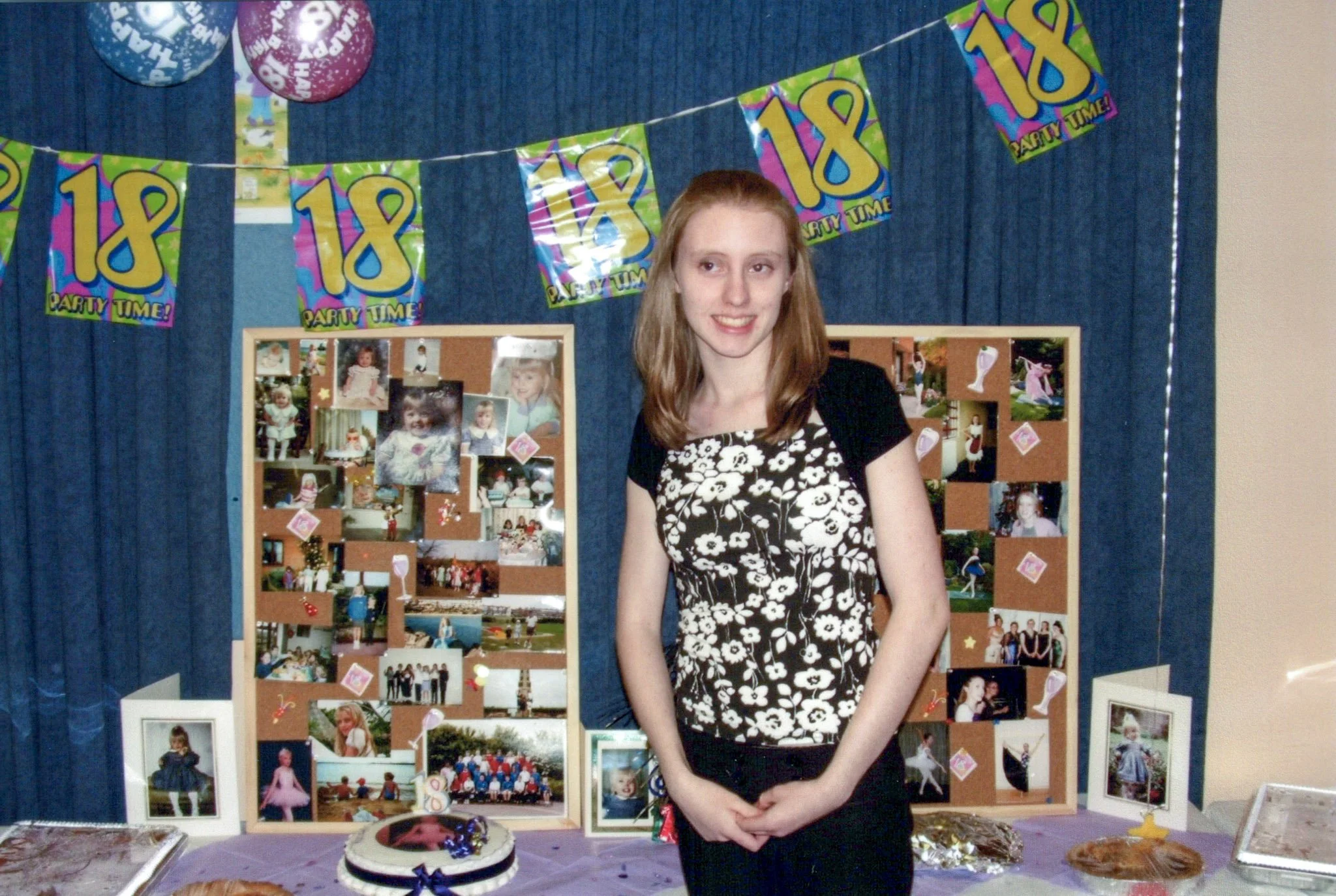 A young woman standing in front of a decorated 18th birthday party display with photos, balloons, and banners.