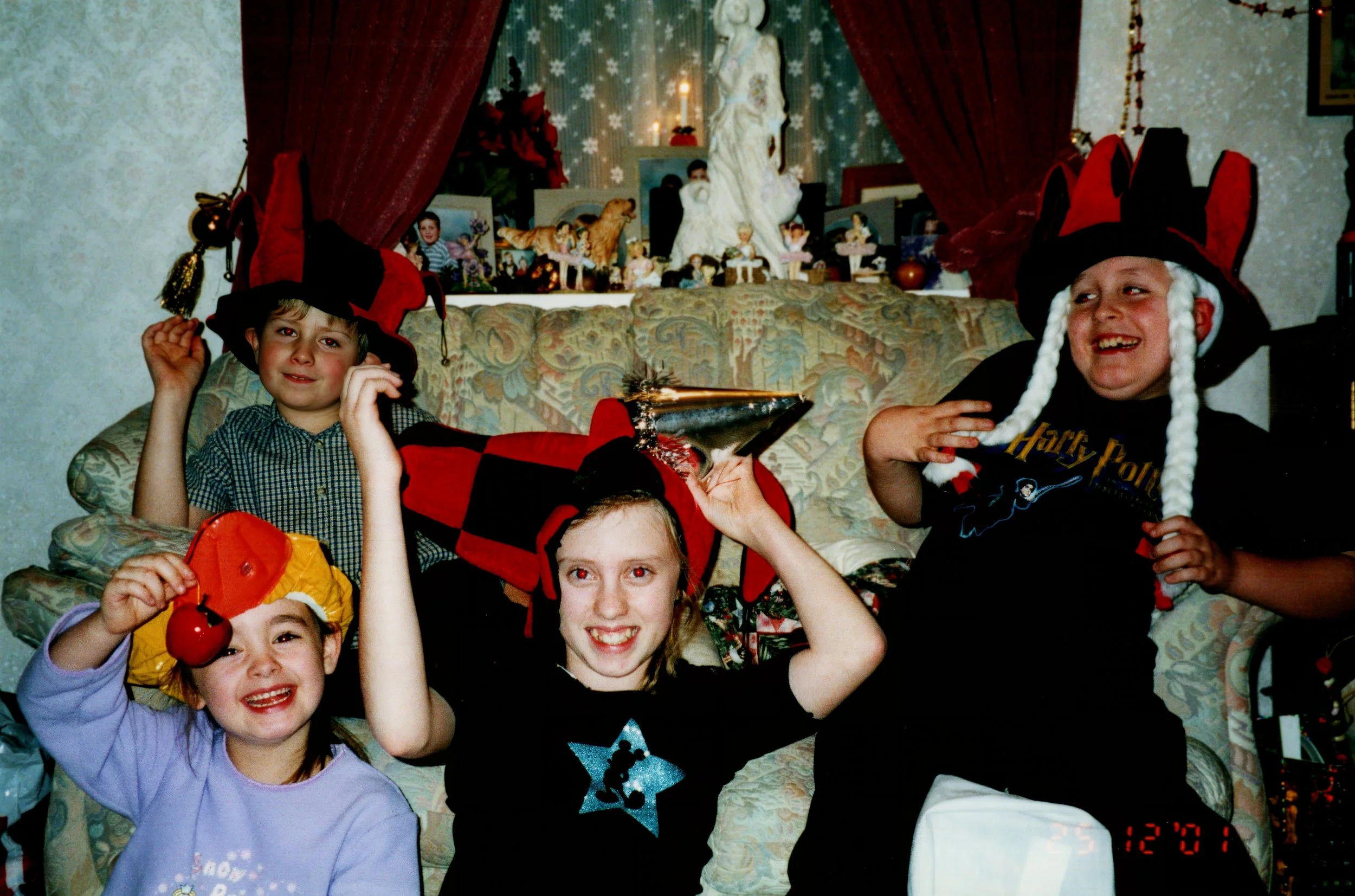 Four children wearing festive hats, sitting on a couch with Christmas decorations in the background.