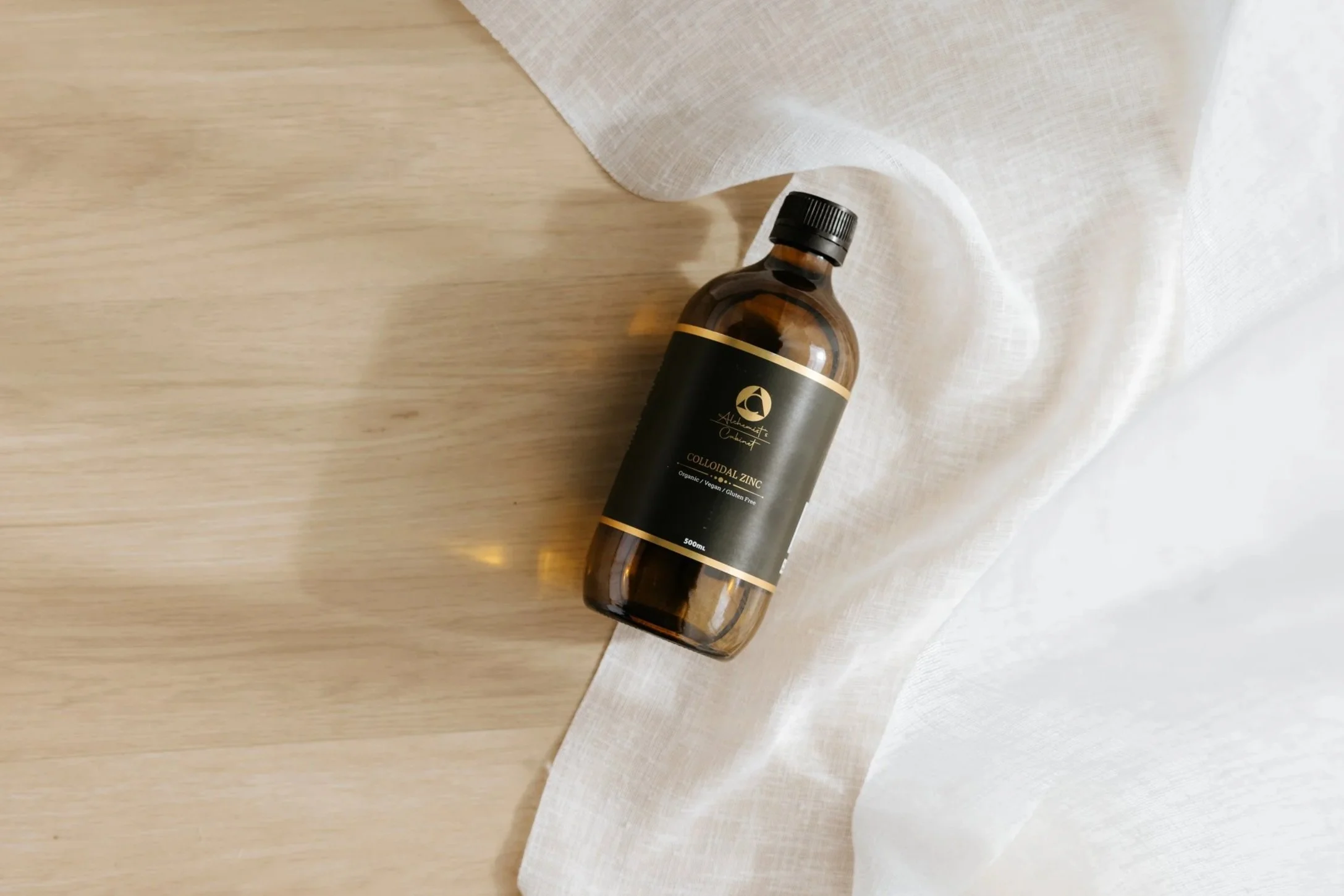 A brown bottle labeled 'Colloidal Zinc' lying on a light wooden surface next to white fabric.