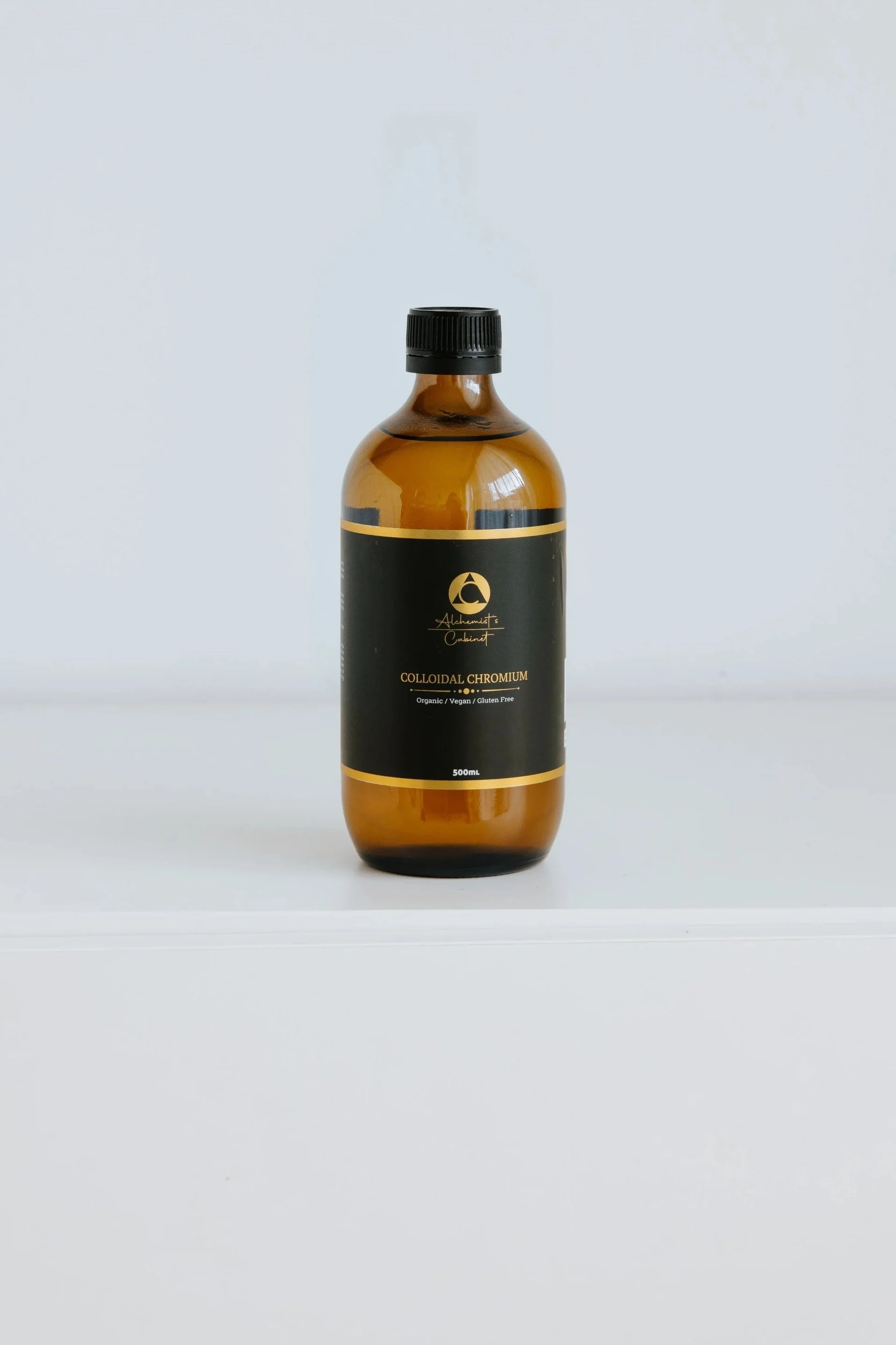 A brown glass bottle labeled 'Alchemist's Cabinet Colloidal Chromium' with a black and gold label, placed on a white surface against a plain light gray background.
