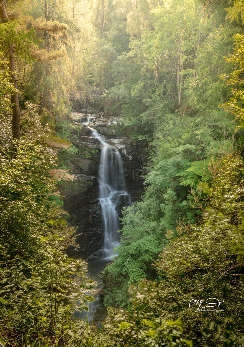 Scottish Central Highlands, Scotland, Perthshire birks of aberfeldy. A scenic waterfall cascading down dark rocks surrounded by lush green trees in a dense forest.