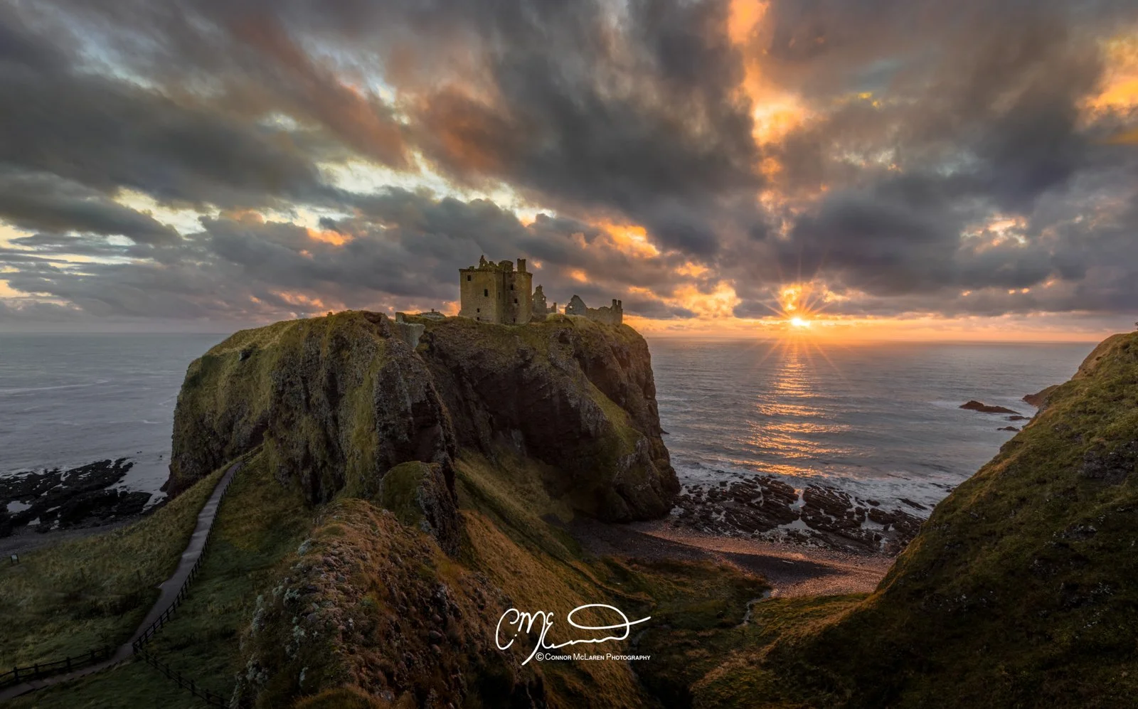 Dunnottar castle, North East Scotland. Sunset over a rugged coastline with a castle on a cliff, waves crashing below, and dramatic clouds in the sky.