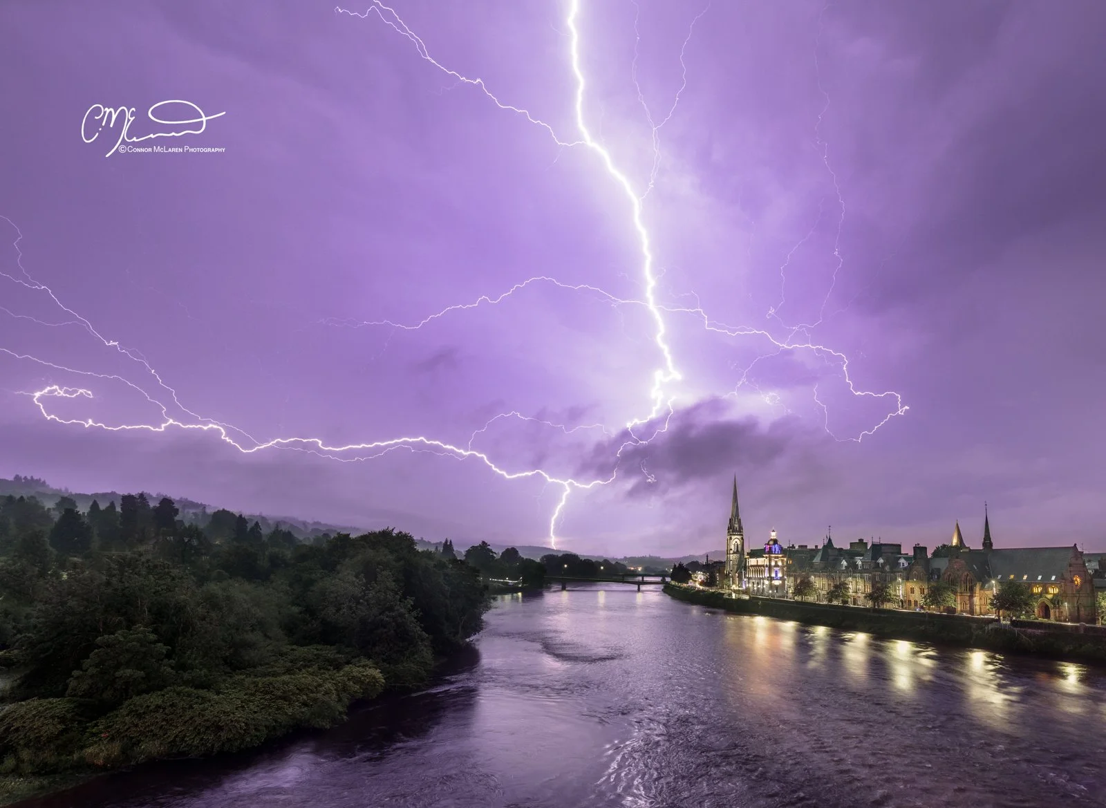Perth Scotland Lightning storm. Lightning storm over a river and a city with historic buildings, illuminated at night, purple sky.
