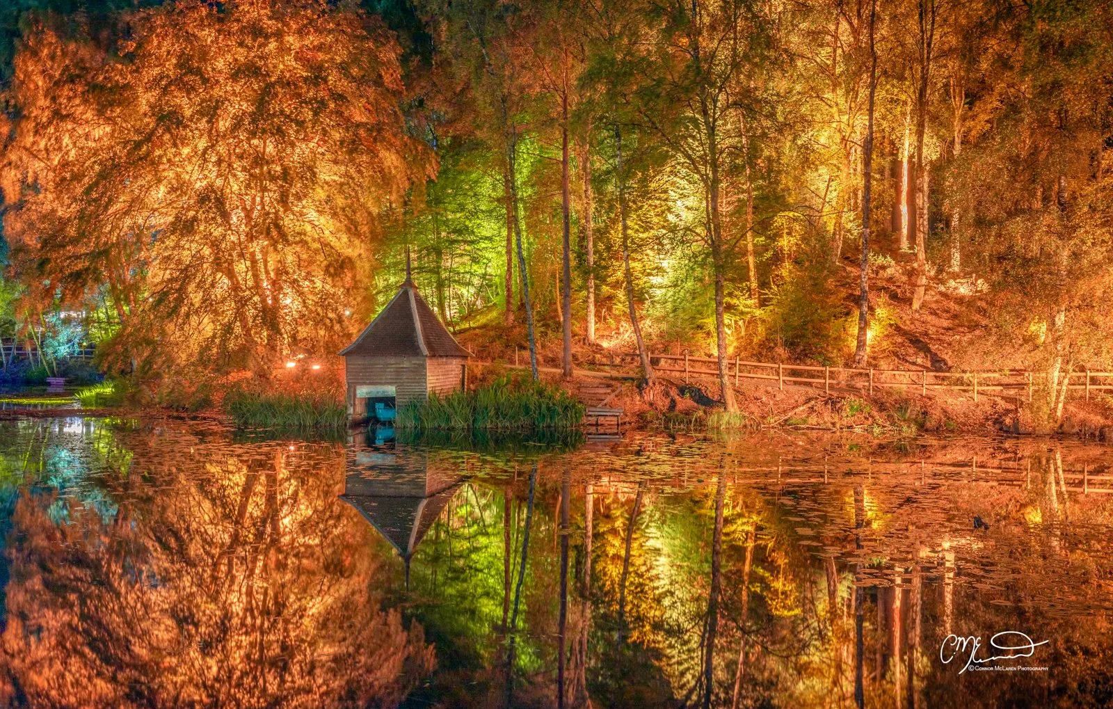 Scottish Central Highlands, Scotland, Perthshire enchanted forest Pitlochry. Night scene of a small wooden lakeside pavilion surrounded by illuminated colorful trees with reflections in the water.