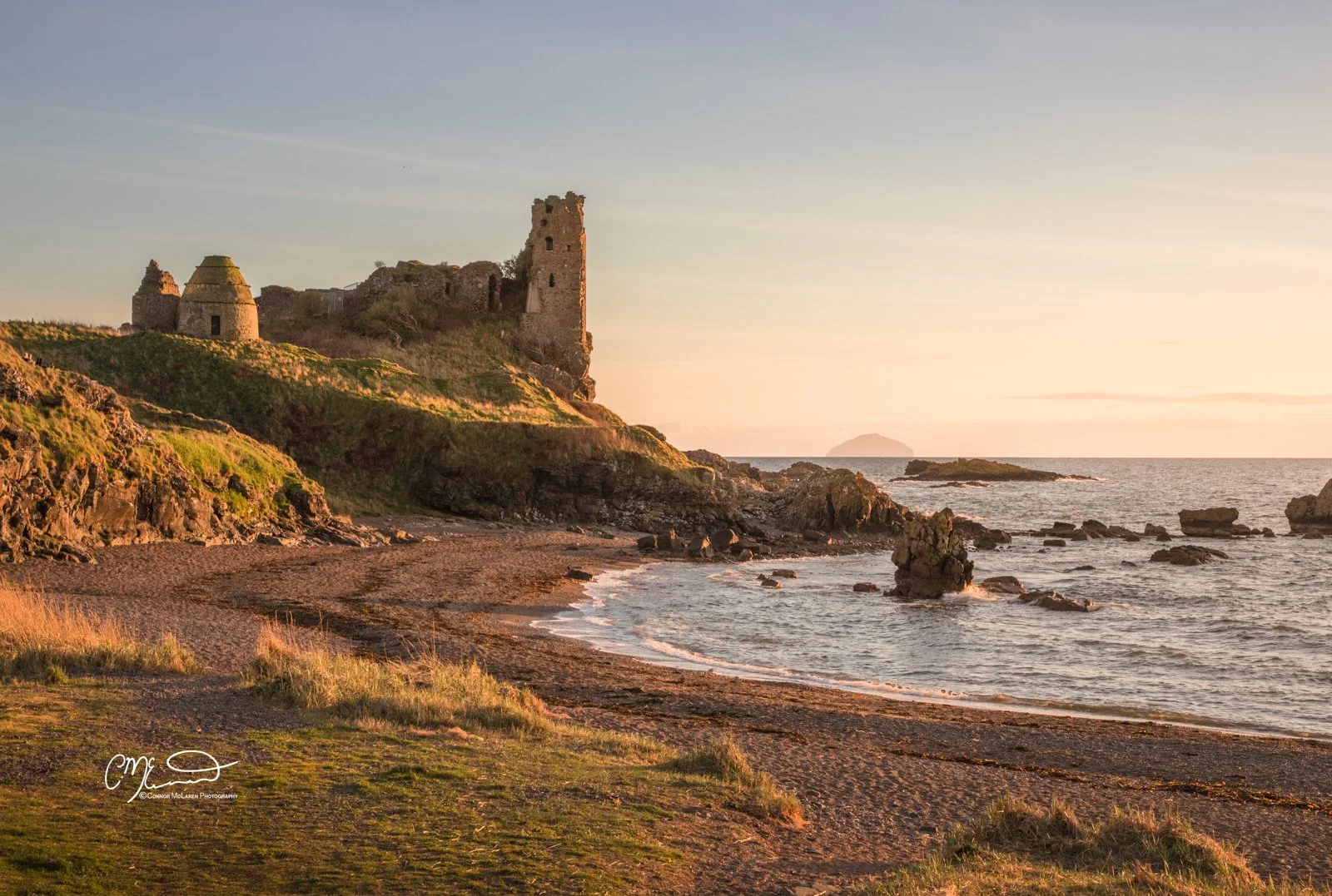 Scottish Lowlands, Scotland, dunure castle. Sunset views of an ancient castle ruins on a grassy hill overlooking a rocky beach and ocean.