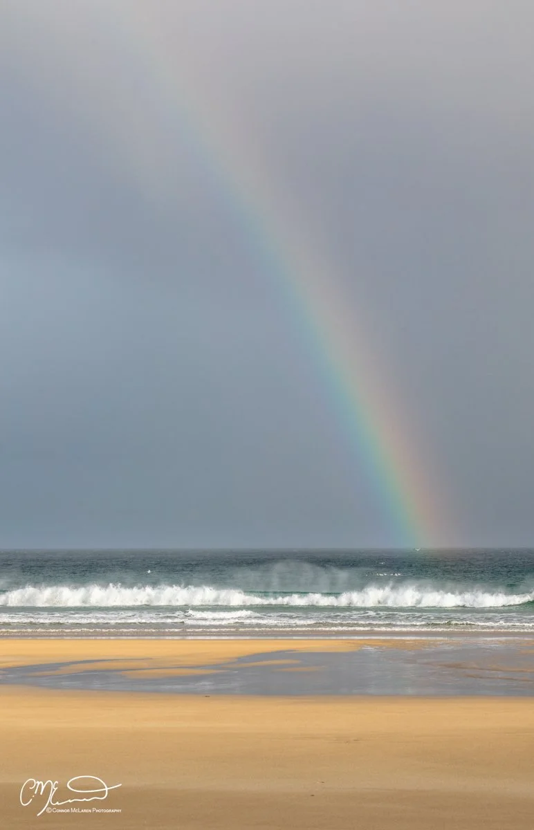 Scotland, Lewis Harris & Outer Hebrides, Tolsta. A rainbow appears over the ocean near a sandy beach on a cloudy day.