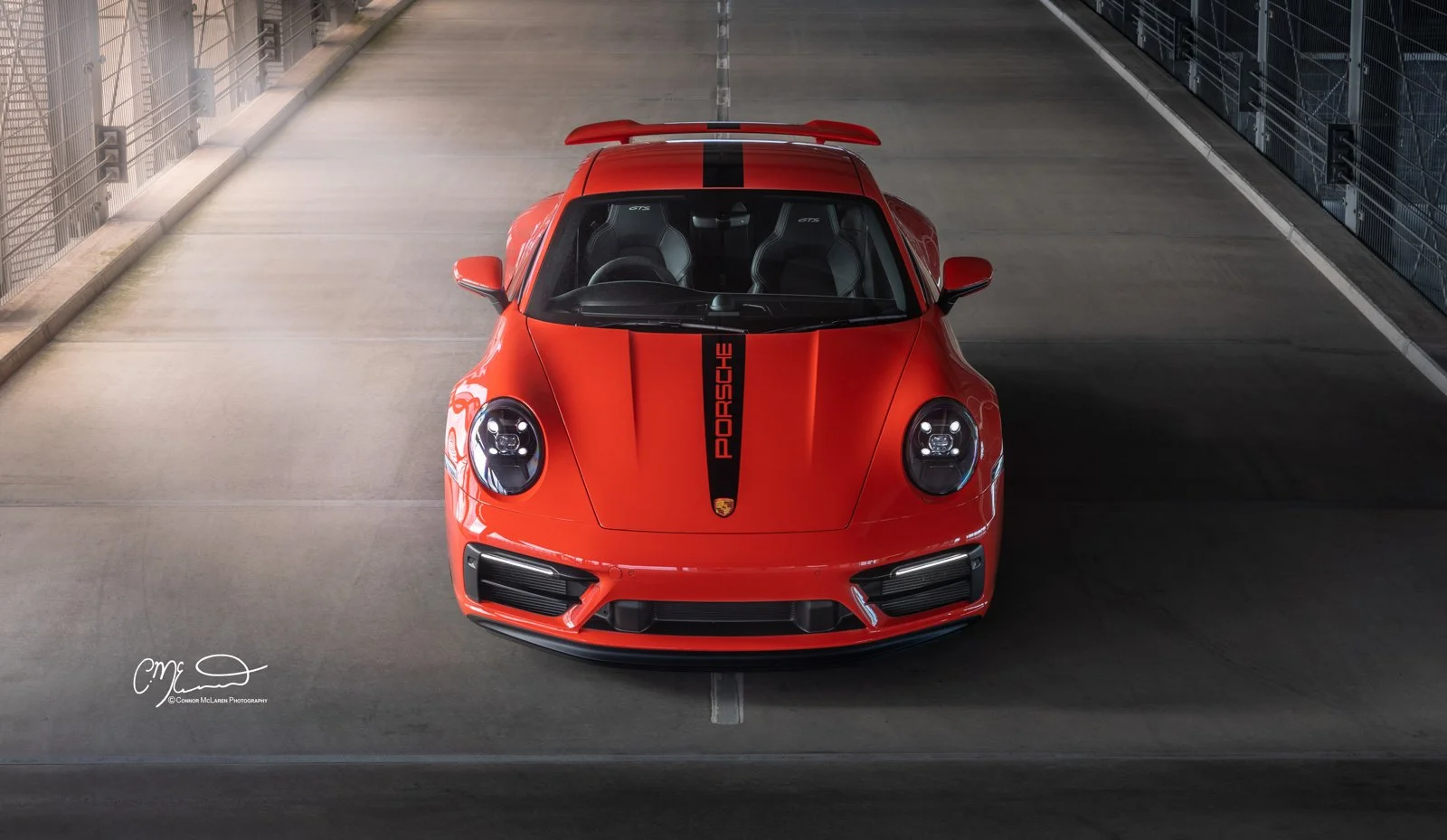 Lava Orange Porsche 911 GTS sports car with black racing stripe in a parking garage, viewed from above.