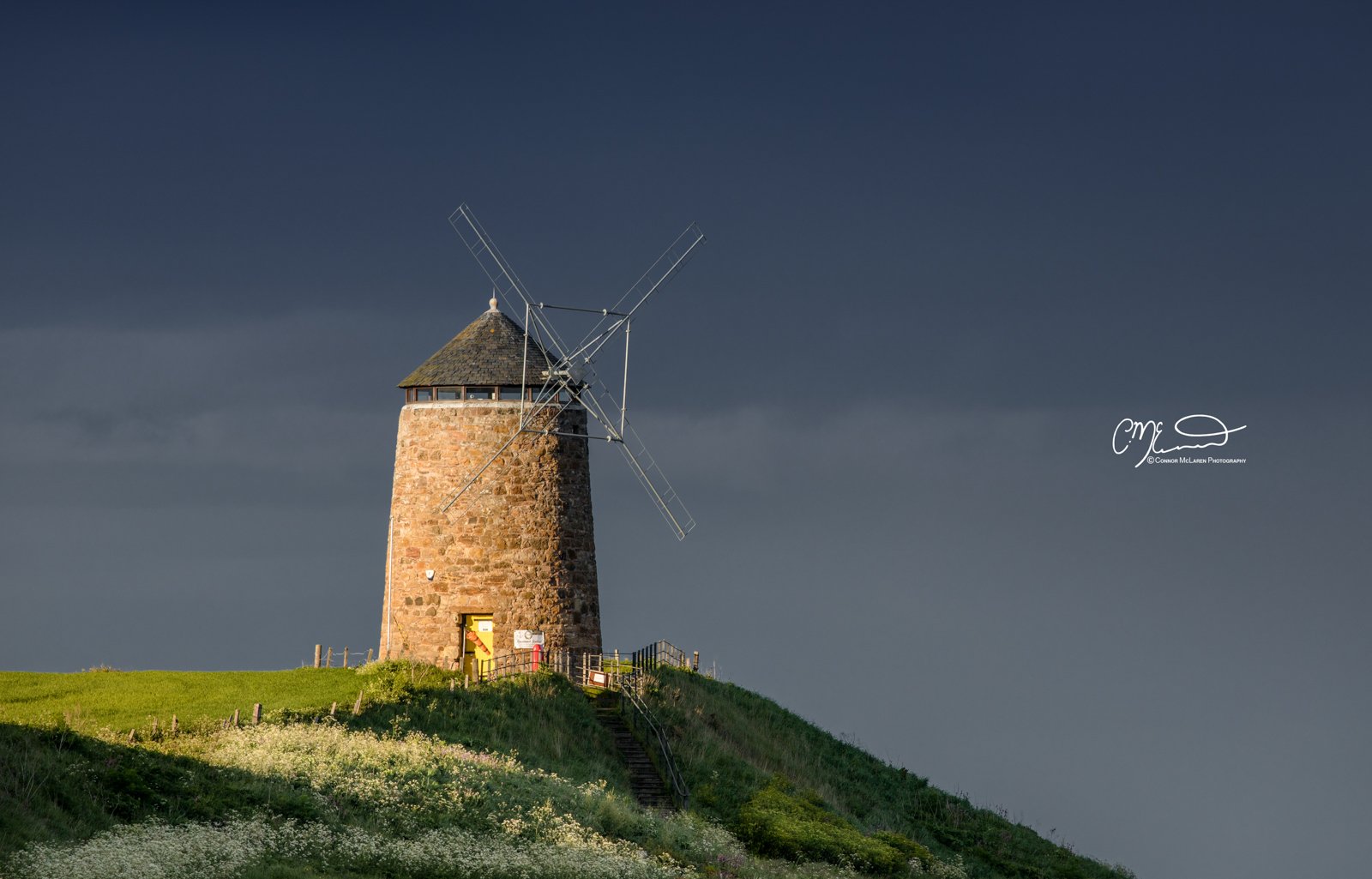 Scottish Lowlands, Scotland, east neuk of fife. A stone windmill on a grassy hill under a dark, cloudy sky.