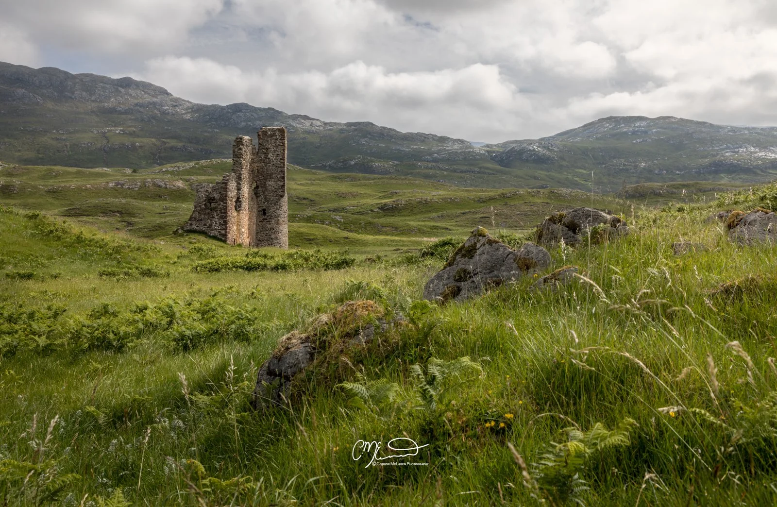 Scotland, north coast 500, NC500, Assynt. ardvrek castle. Ruins of an old stone castle or structure in a green field with rolling hills and mountains in the background under cloudy sky.