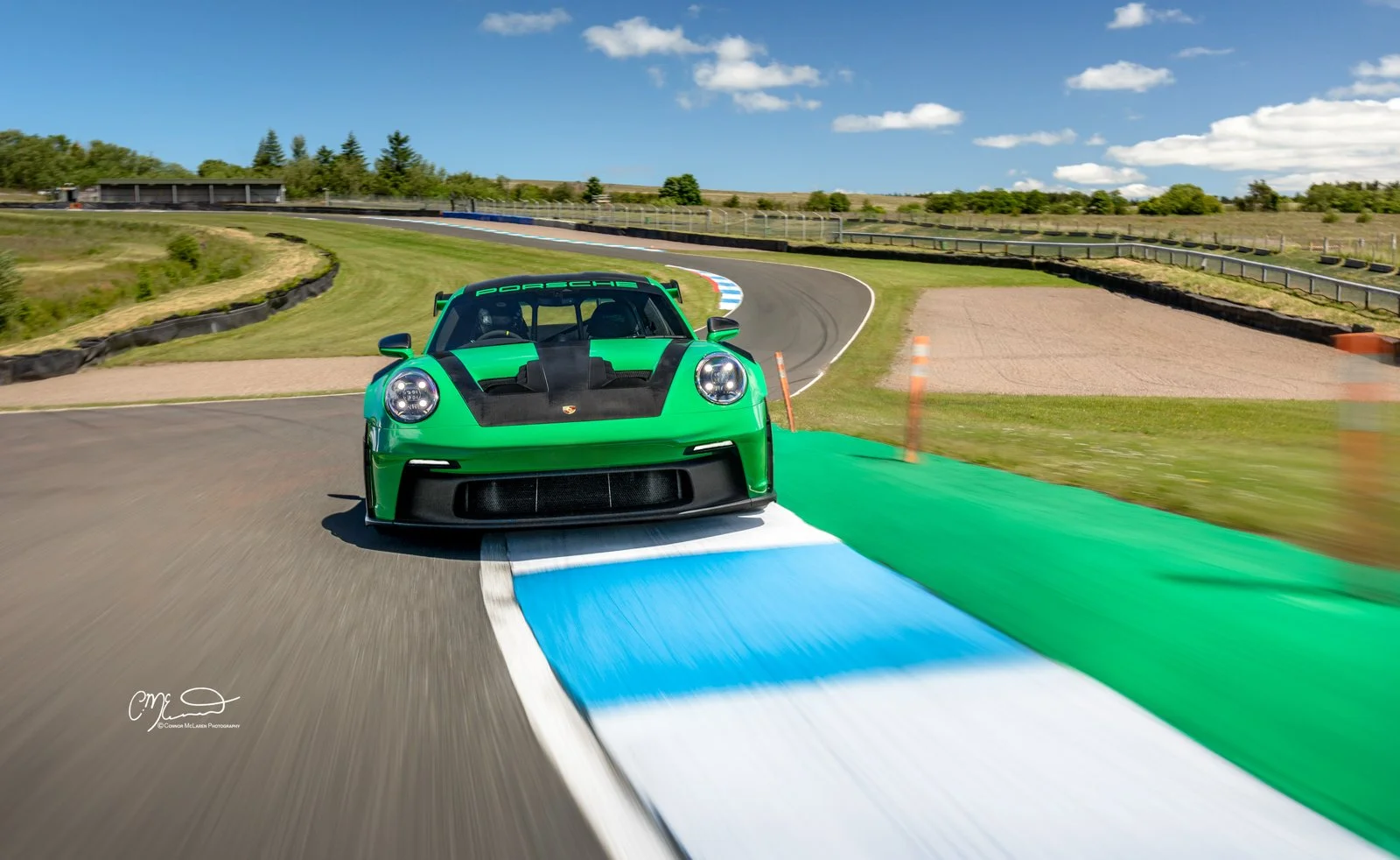 Porsche 911 GT3 RS Weissach in Python Green at Knockhill racing. Amazing photograph, wallpaper. Green race car on a racetrack with blue, white, and green painted curbs under a partly cloudy sky.