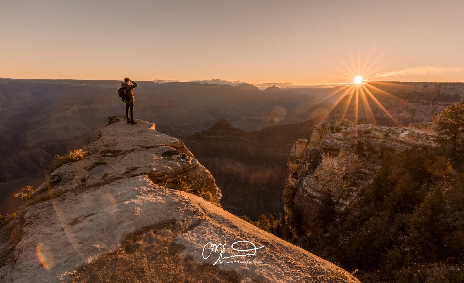 Grand Canyon, south rim, Arizona AZ, united states of america, usa. A person with a backpack standing on a rocky edge overlooking the Grand Canyon at sunset, taking in the view with the sun setting on the horizon.