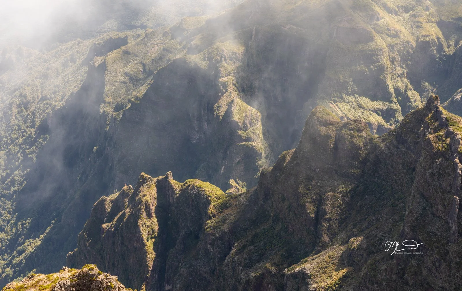 Pico do Arieiro mountain top, Madeira Portugal. Mountain landscape with rugged peaks, lush green slopes, and mist or clouds in the background.