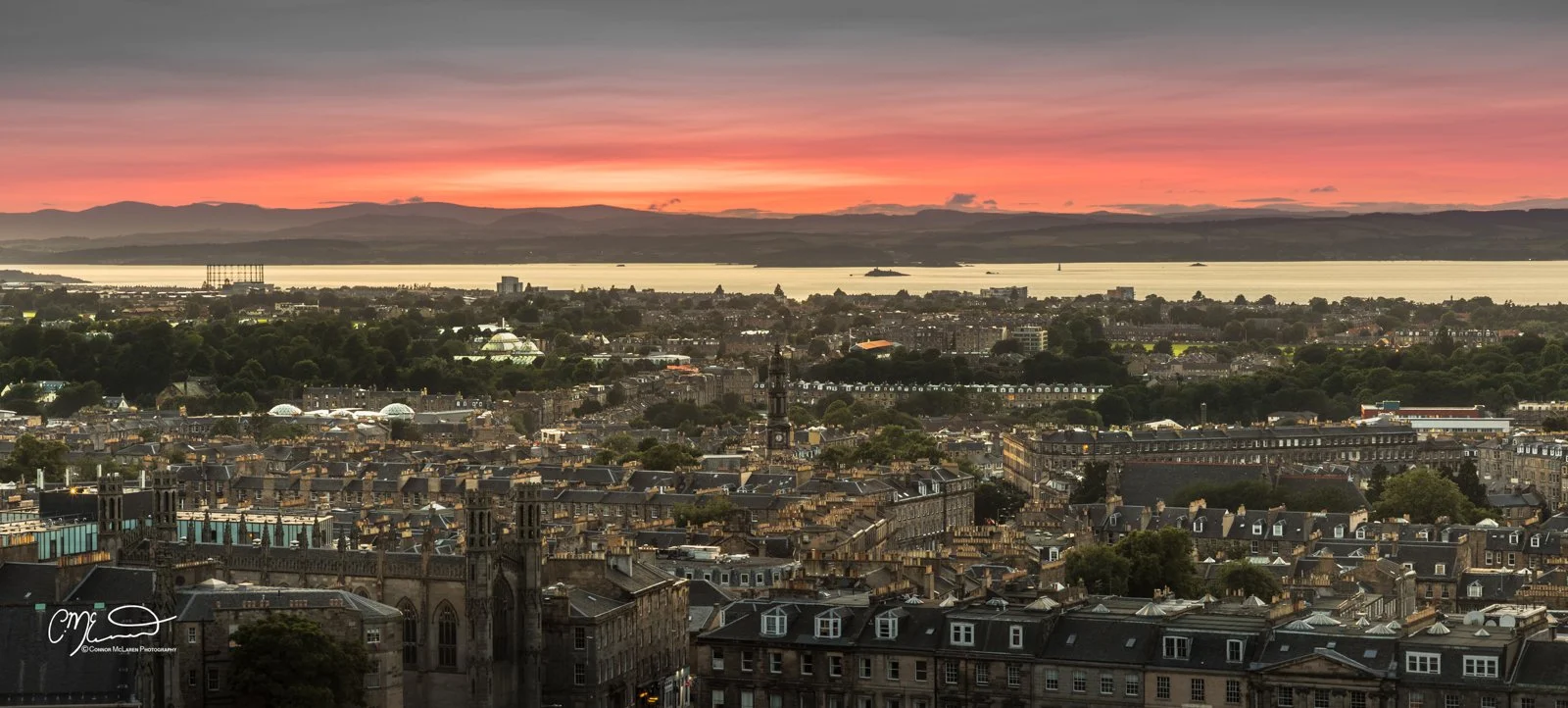 Scottish Lowlands, Scotland,  Edinburgh. A cityscape at sunset with a body of water and mountains in the distance.
