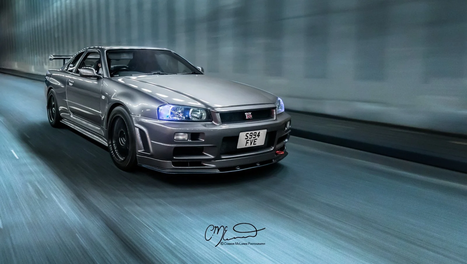 A silver Nissan Skyline GT-R R34 driving through a tunnel at night.