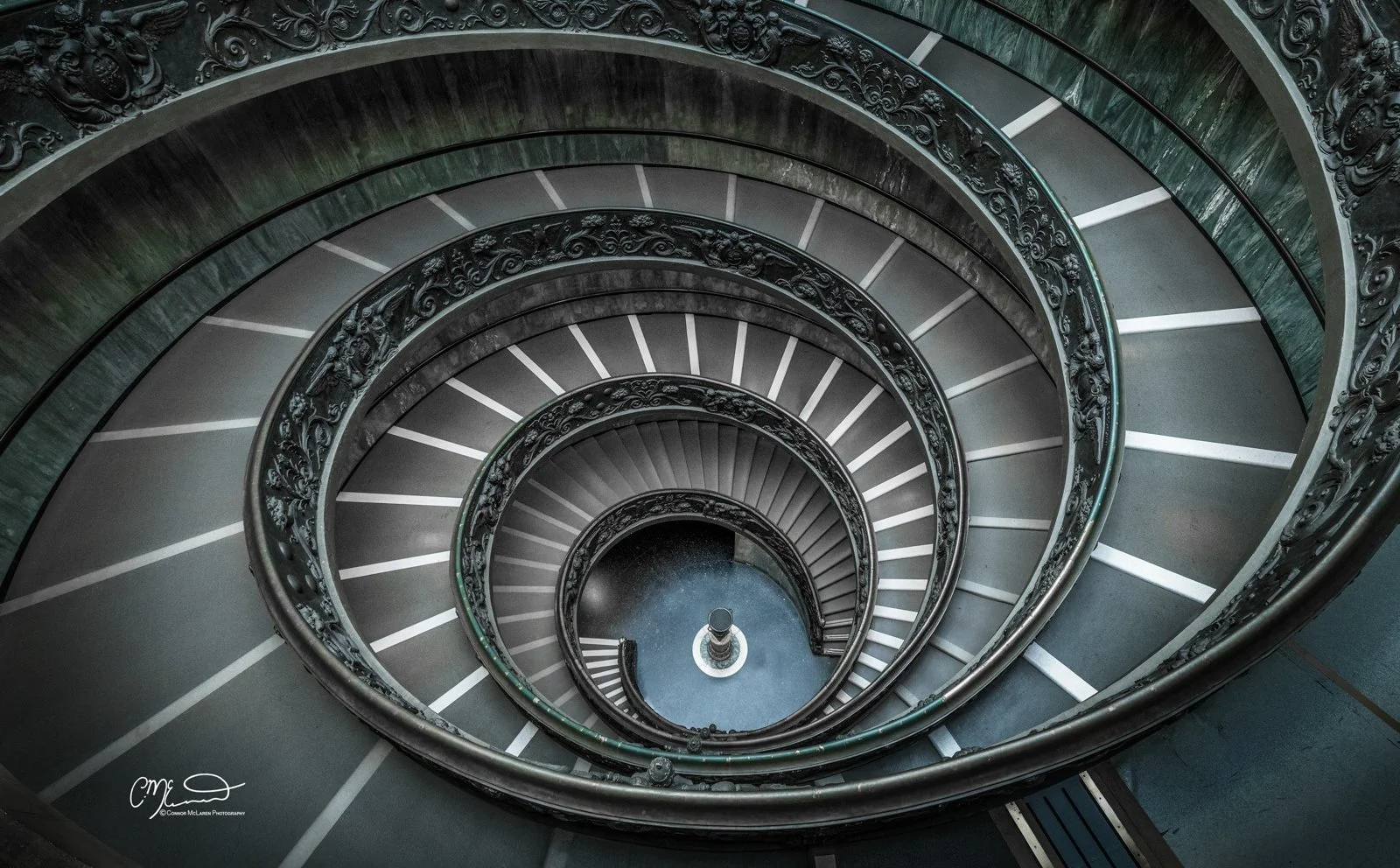 Bremante stairs, Roman Forum and colosseum, Rome & the vatican. Spiral staircase seen from above, featuring ornate black railings and steps that gradually descend in a circular pattern.